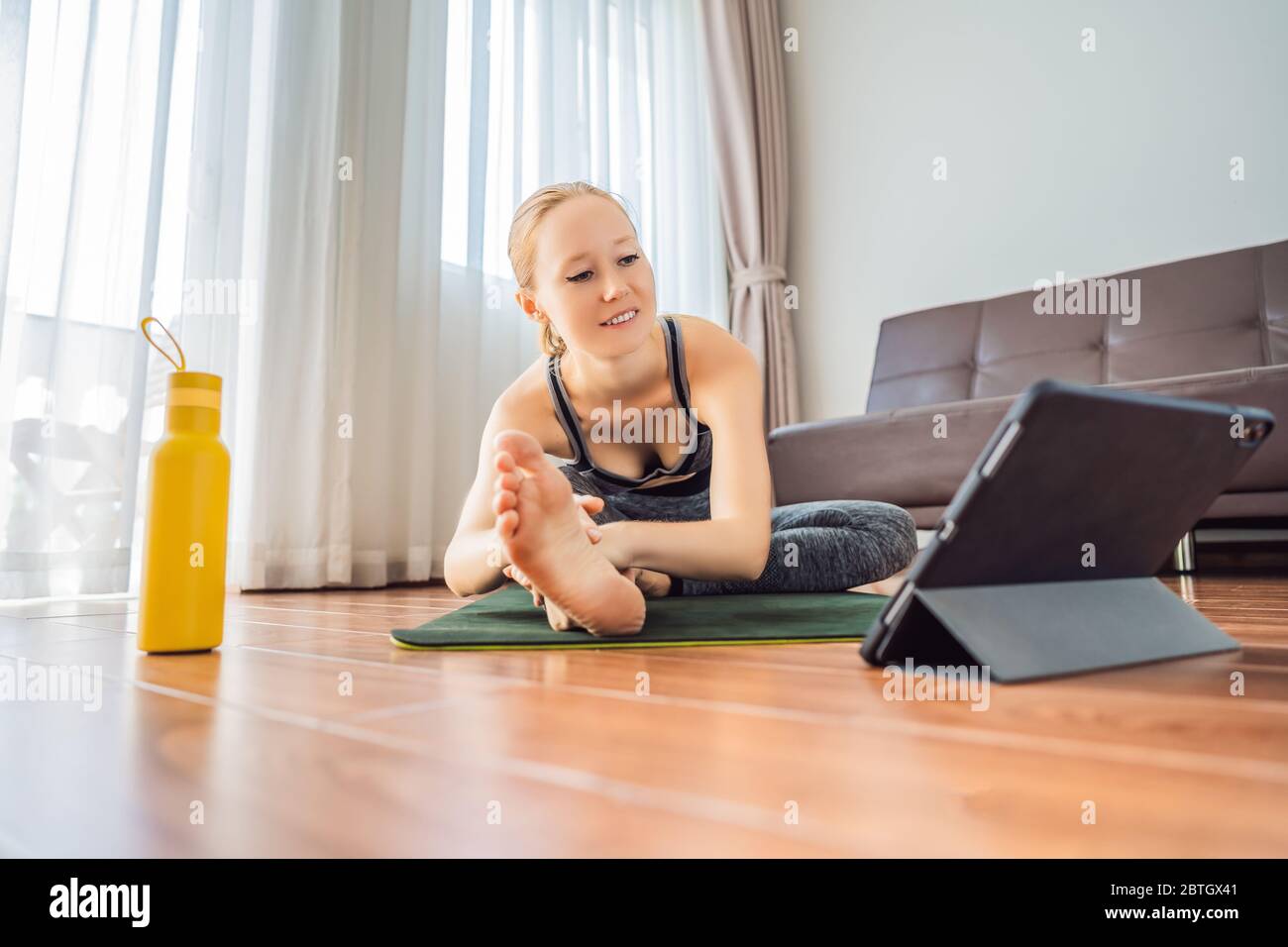 Donna che si esercita sul pavimento a casa e guarda i video di fitness in un tablet. La gente fa sport in linea a causa del coronovirus Foto Stock