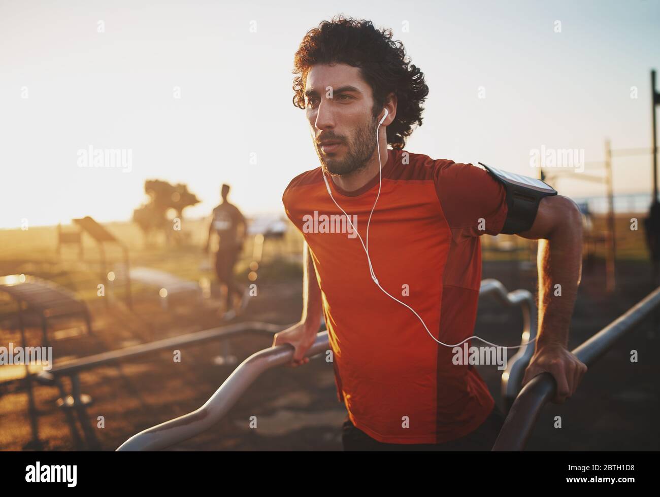 Ritratto di un giovane atletico che ascolta musica sulle cuffie facendo esercizio su barre parallele nel parco - giovane uomo che fa un'immersone all'aperto Foto Stock