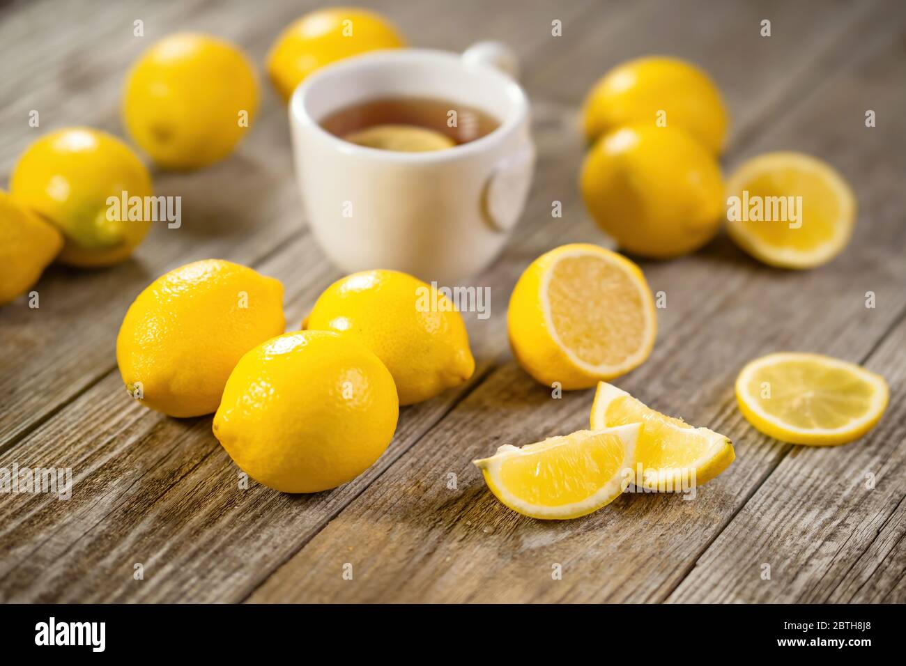 Tazza di tè nero con fetta di limone e abbondanza di limoni intorno su tavola di legno grigio. Infusione di bevande calde per le giornate di caduta e d'inverno. Foto Stock