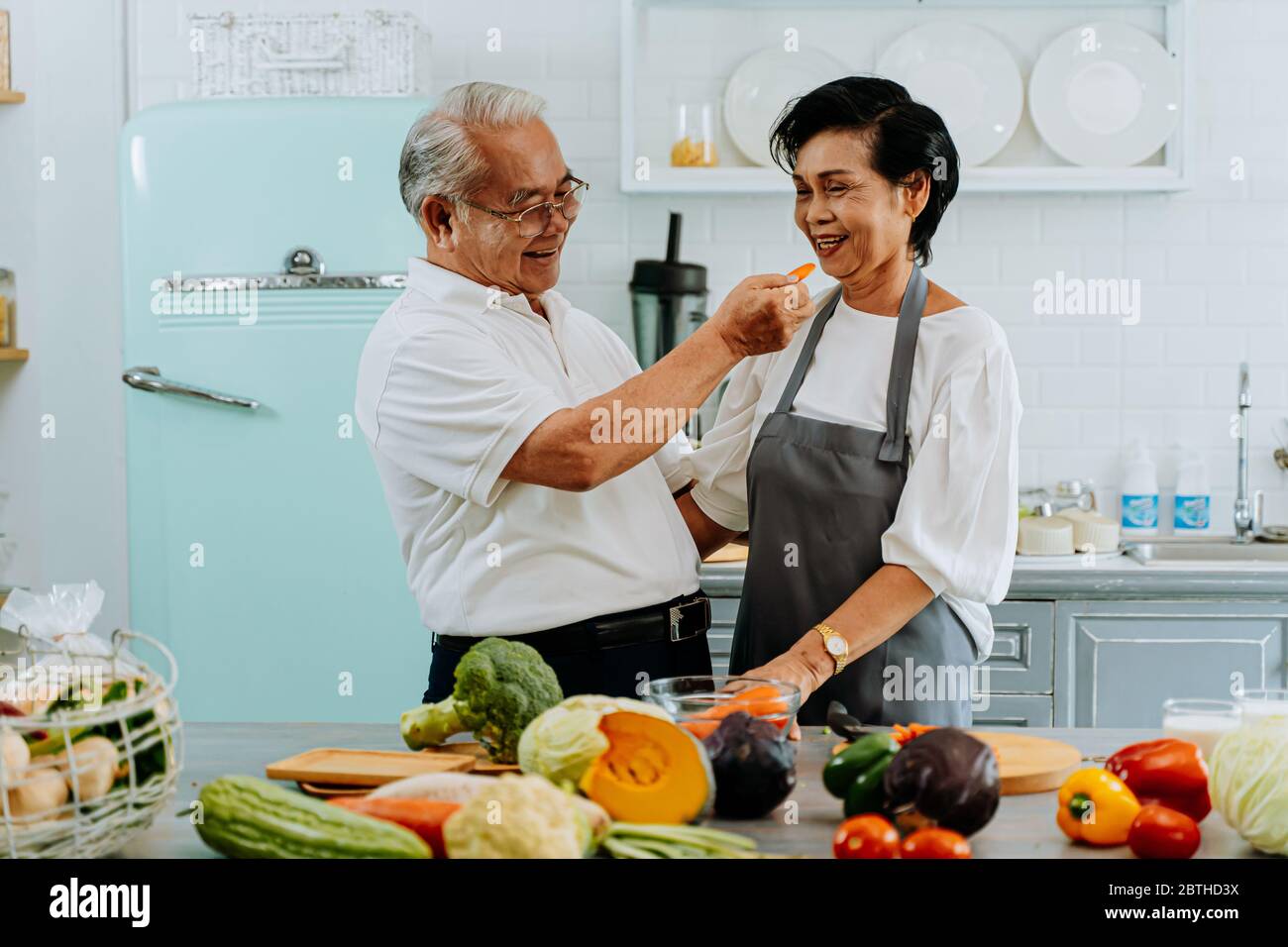 Senior Asian giovane nonni cucinare insieme mentre la donna è la alimentazione cibo per l'uomo in cucina. Relazione di lunga durata concetto Foto Stock