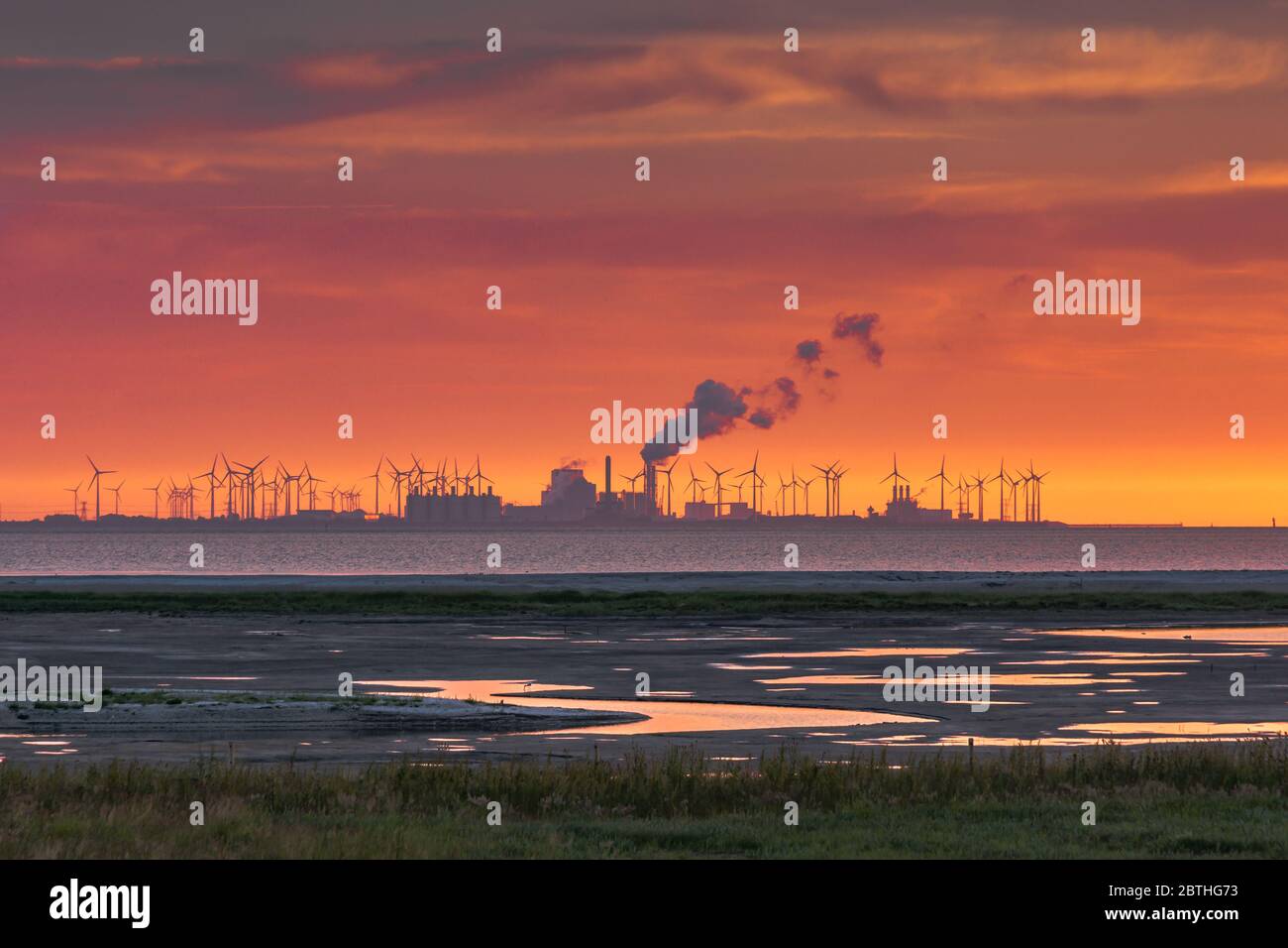 Tramonto sul mare di Wadden, vista degli edifici di fabbriche e turbine eoliche di Eemshaven, Paesi Bassi Foto Stock