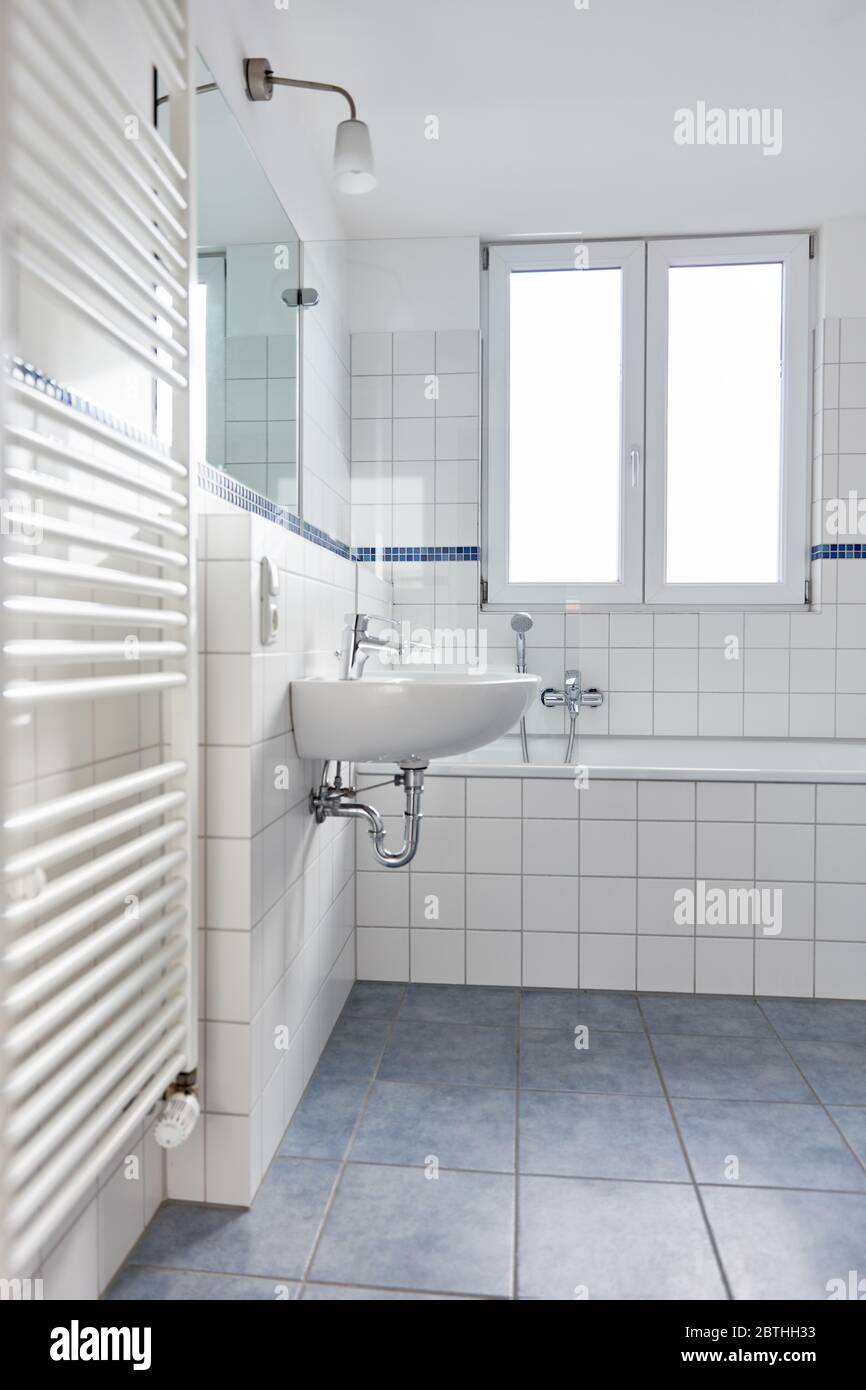 Bagno moderno e luminoso con piastrelle bianche, radiatori tubolari e vasca Foto Stock