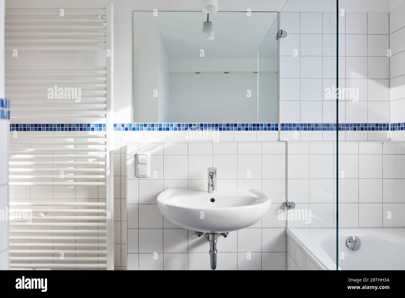 Bagno luminoso e bianco con lavello e specchio e radiatore accanto alla vasca Foto Stock