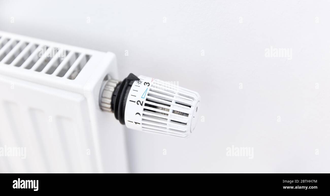 Stufa bianca con radiatore e termostato moderno sulla parete in un appartamento Foto Stock