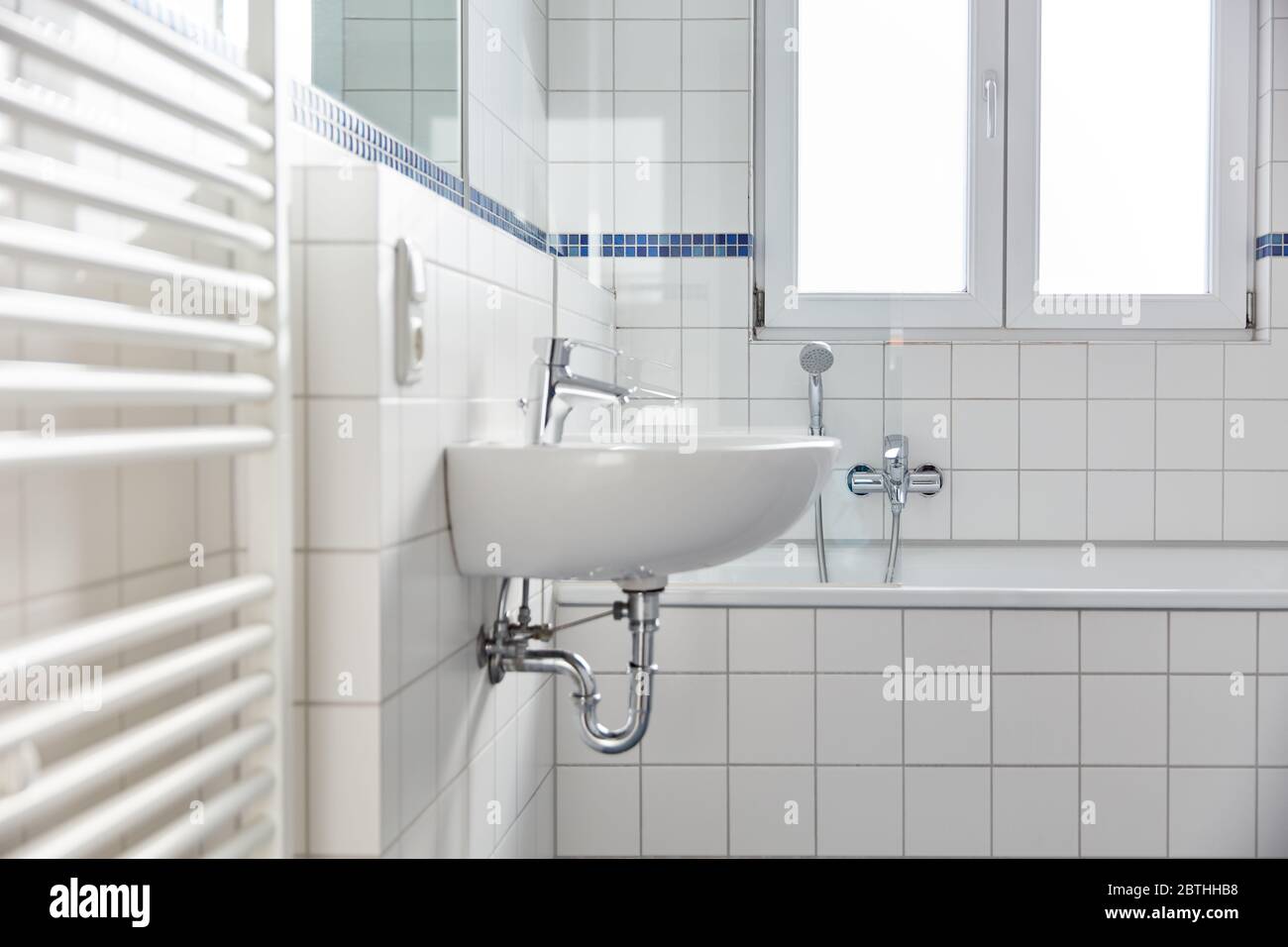 Bagno bianco luminoso con lavello e vasca accanto a radiatori tubolari a casa Foto Stock