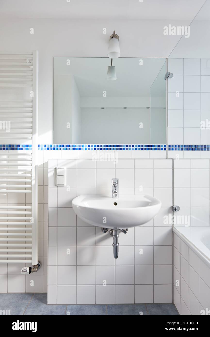 Lavandino con specchio in bagno bianco luminoso accanto al radiatore tubolare a casa Foto Stock
