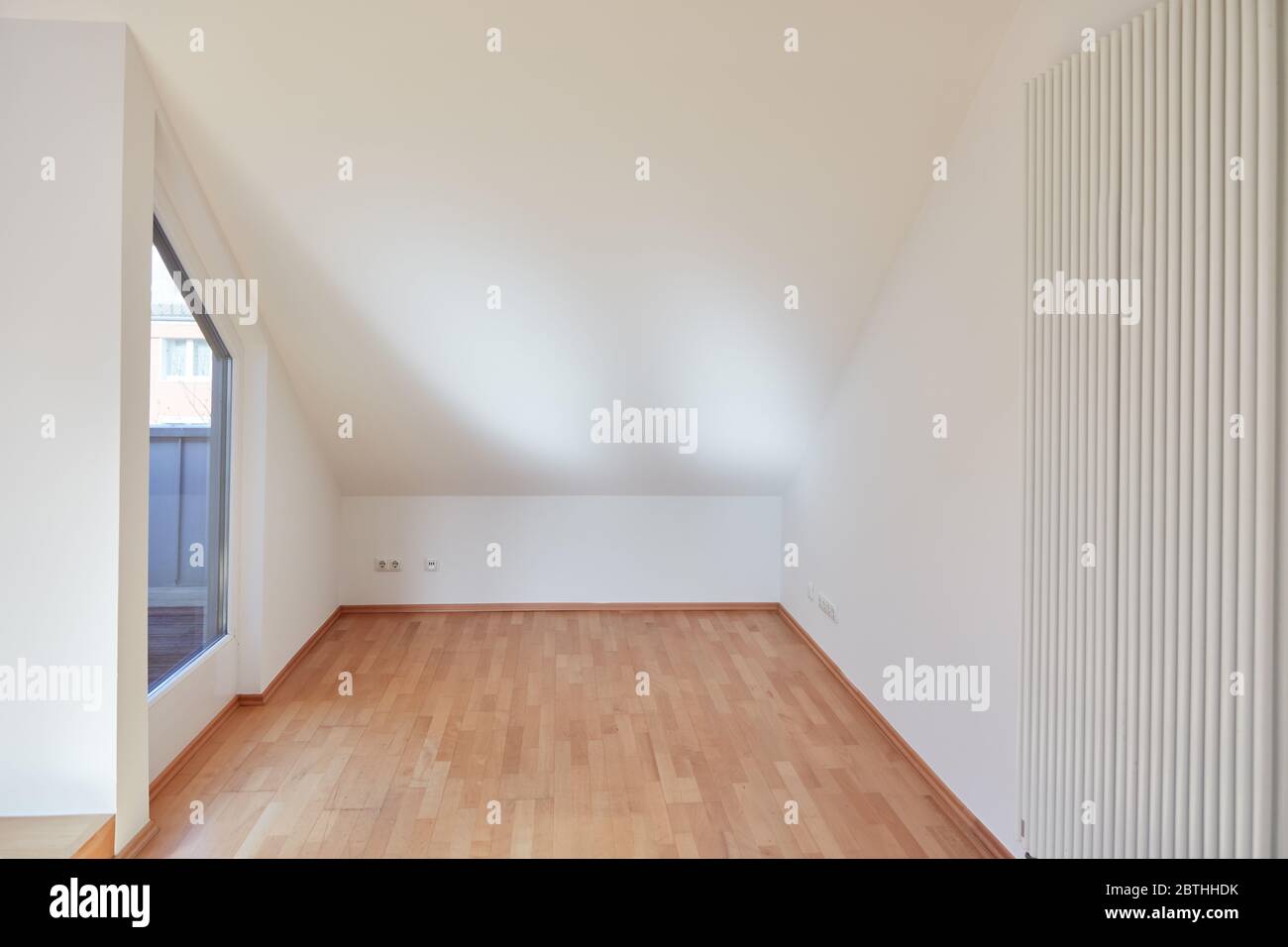 Camera vuota con soffitti inclinati e parquet in legno duro in un nuovo appartamento mansardato Foto Stock