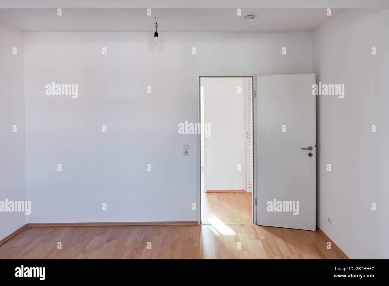 Porta aperta e parete bianca in camera vuota con parquet in legno duro a casa Foto Stock