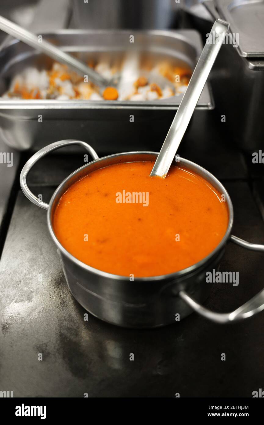 Zuppa gialla in un recipiente di metallo. Preparazione del pranzo nella sala da pranzo. Stufato esotico. Cibo in una piastra di acciaio. Foto Stock