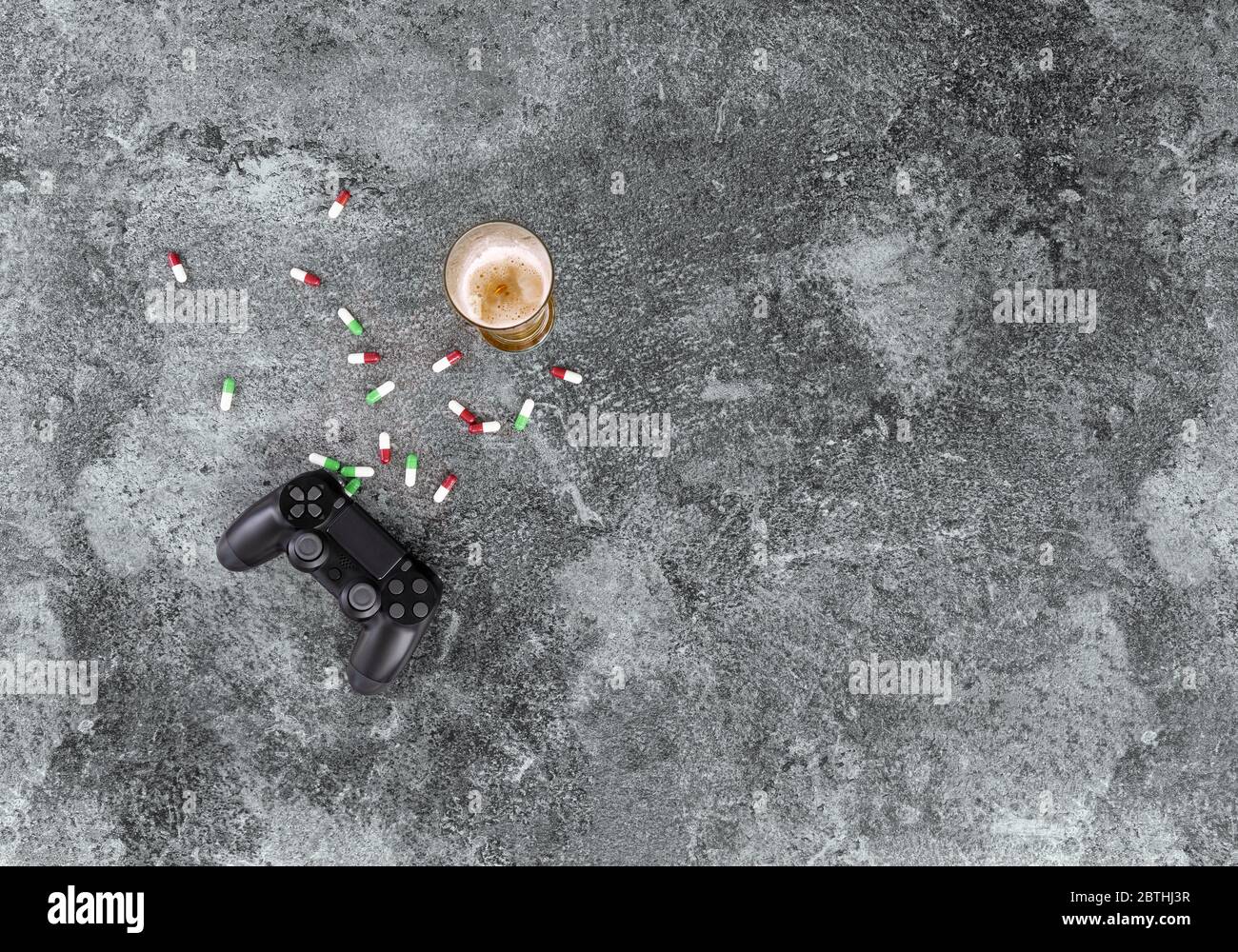 il consumo eccessivo di alcol, droghe, medicinali e giochi per computer danneggia la salute, il controller di gioco, il bicchiere da birra e le pillole su un tavolo in marmo grigio Foto Stock