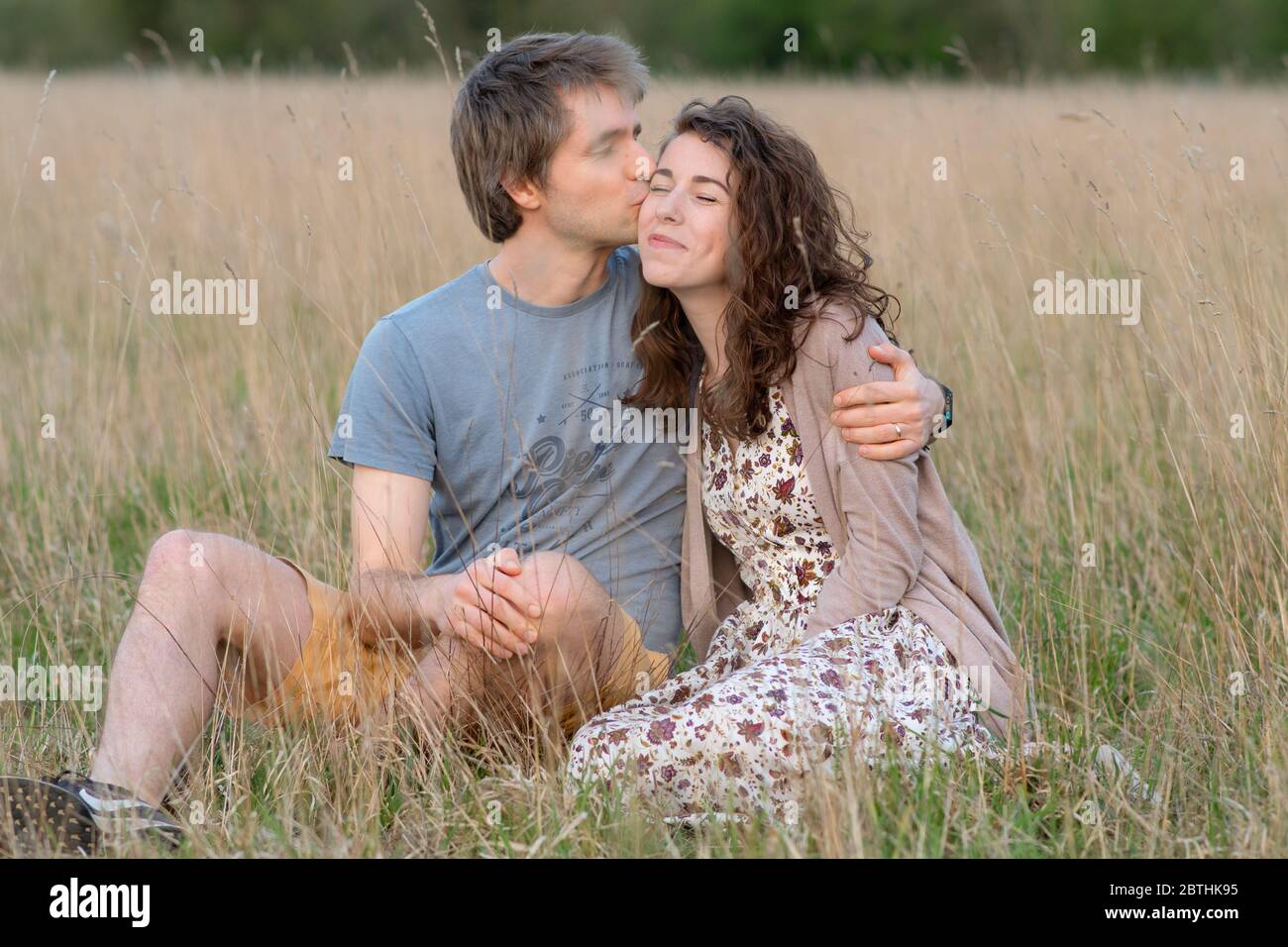 Una giovane bella coppia sorridere insieme in un bel campo esterno mostrando il loro amore per l'altro e baciando Foto Stock