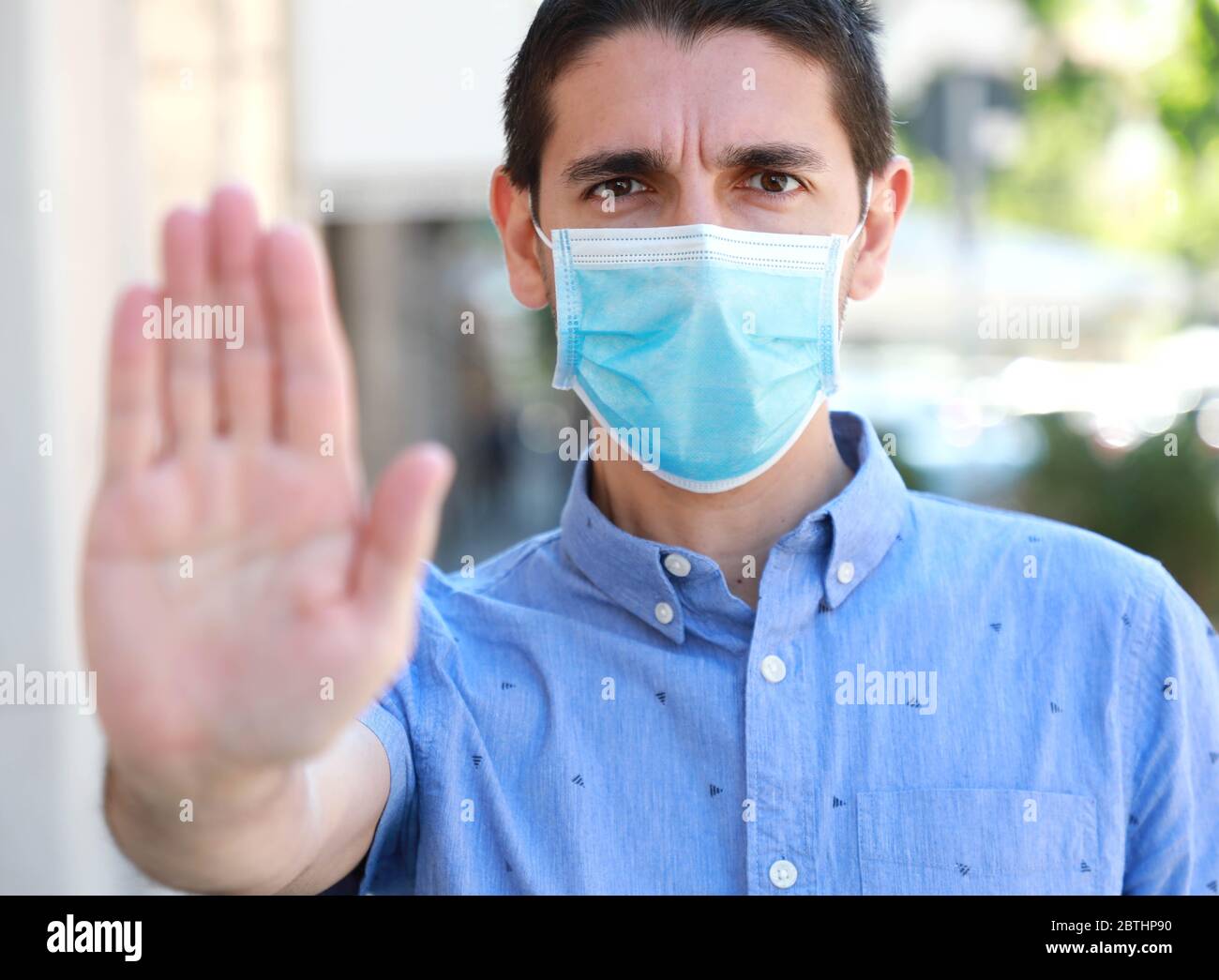 FERMARE COVID-19 uomo che indossa la maschera chirurgica sul viso facendo GESTO DI ARRESTO guardando la fotocamera all'esterno. Giovane uomo con maschera che mostra palmo aperto della mano al Foto Stock