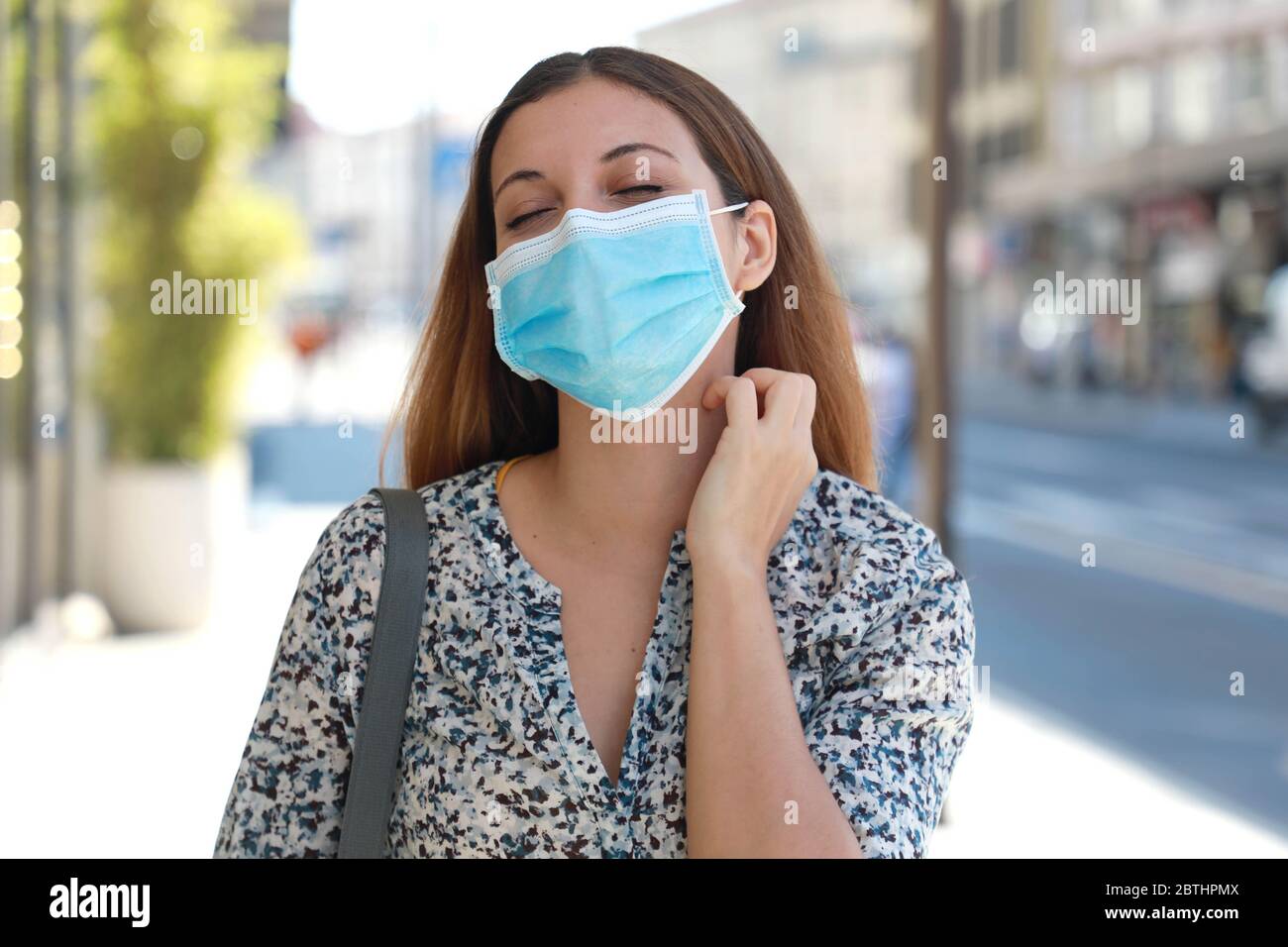 Giovane donna con maschera chirurgica prurito sintomi allergici graffiare il collo in città strada Foto Stock