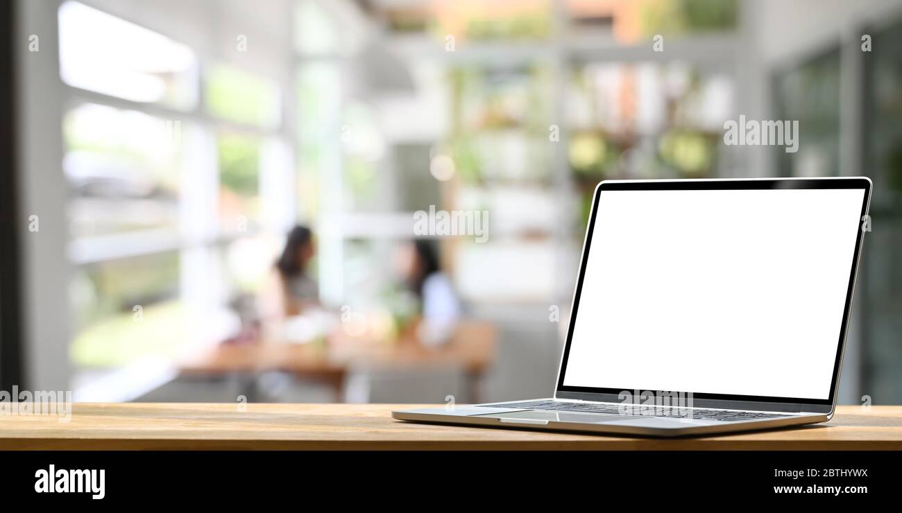 Foto di bianco schermo bianco computer portatile mettere su bancone bar di legno su un ristorante confortevole e clienti come sfondo. Foto Stock