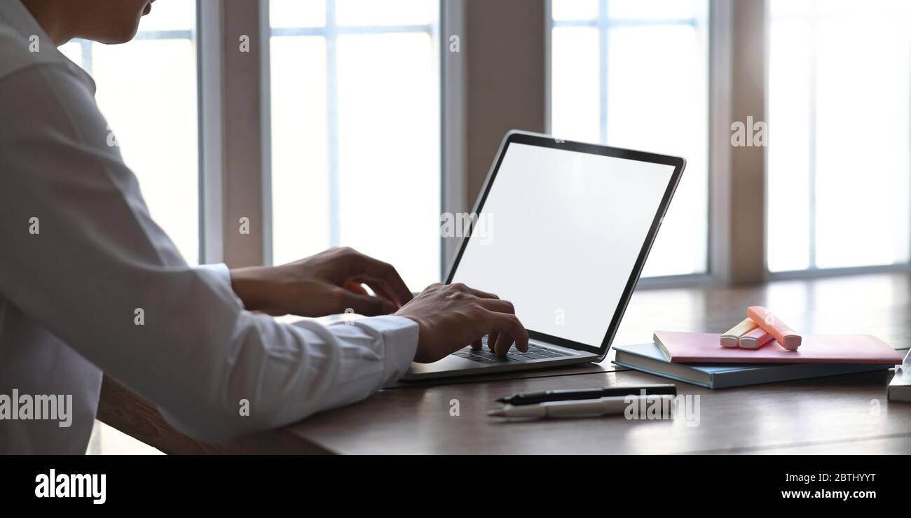 Foto di un uomo intelligente che lavora come contabile mentre si è seduti e lavora con un computer portatile bianco a schermo vuoto alla scrivania in legno che circondava Foto Stock