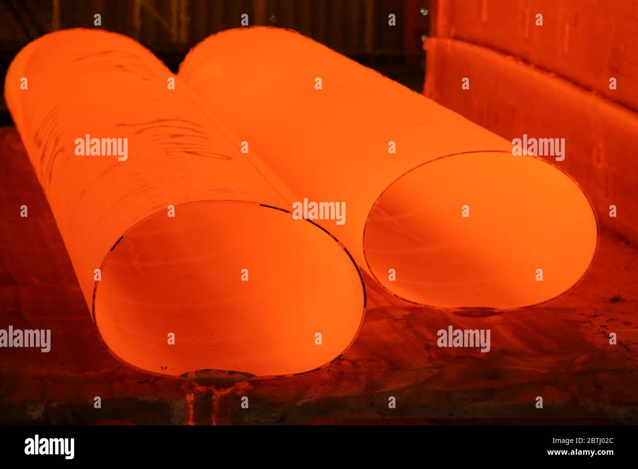 Grandi tubi di acciaio rosso caldo che escono dal laminatoio e formatore Foto Stock
