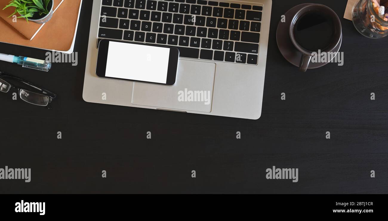 Immagine dall'alto del computer portatile che si trova su una scrivania nera e circondato da schermo bianco mobile, bicchieri, matite, caffè in ceramica, sta Foto Stock