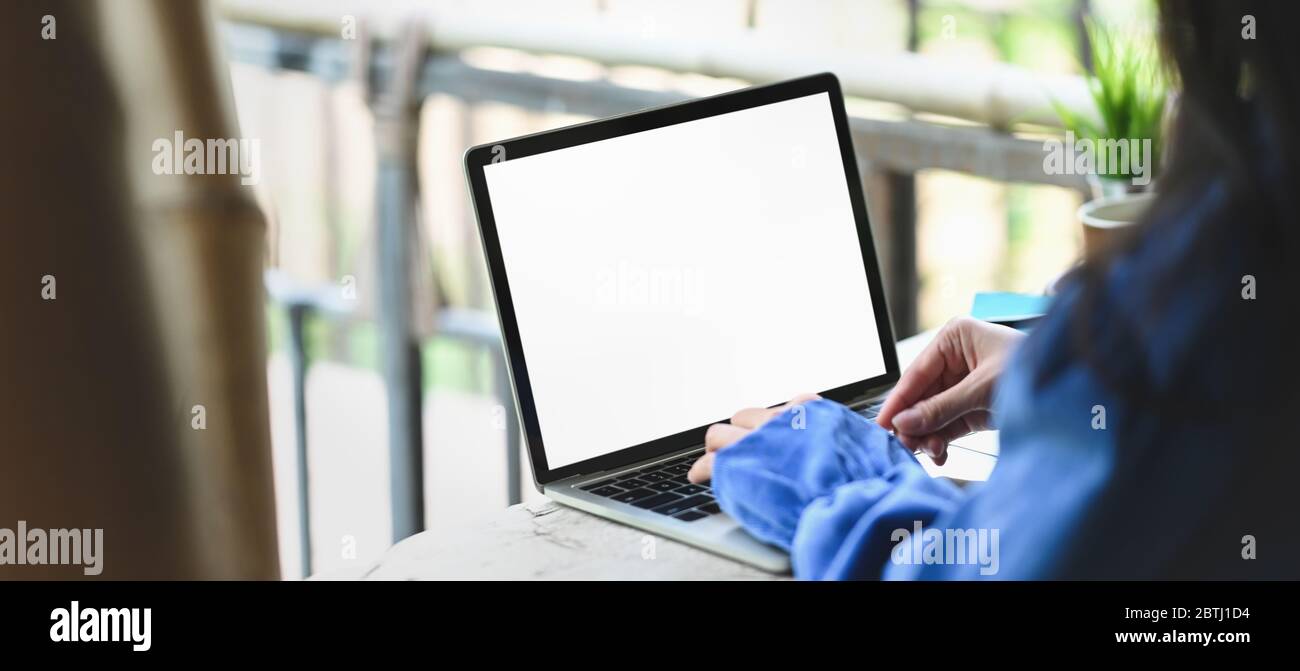 Immagine ritagliata delle mani della donna che scrivono su bianco schermo computer portatile bianco che mettere su banco di legno vintage barra sopra balcone vista come b Foto Stock