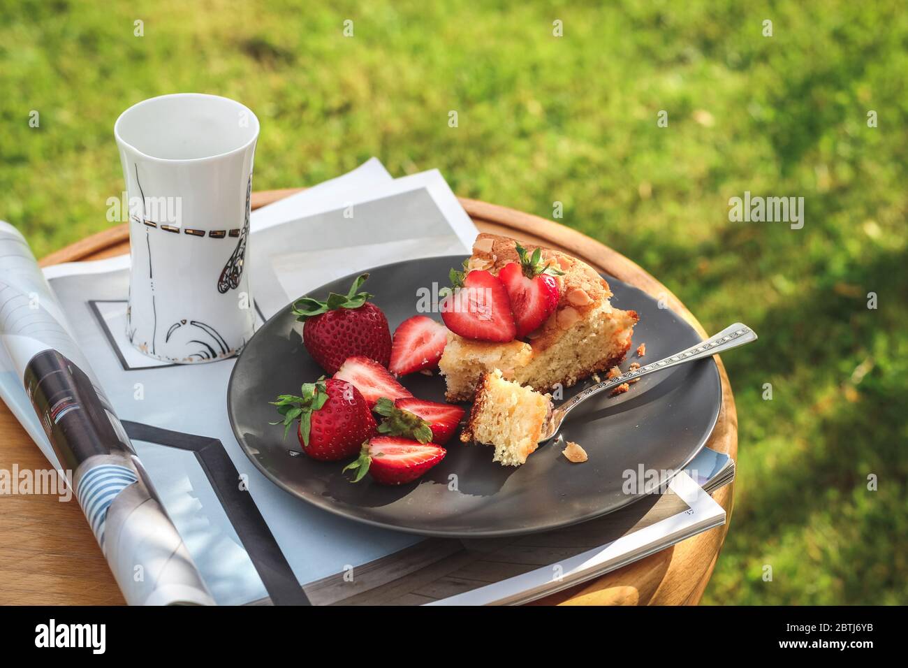 Una fetta di torta fatta in casa con fragole e una tazza di caffè su uno sgabello in un giardino Foto Stock