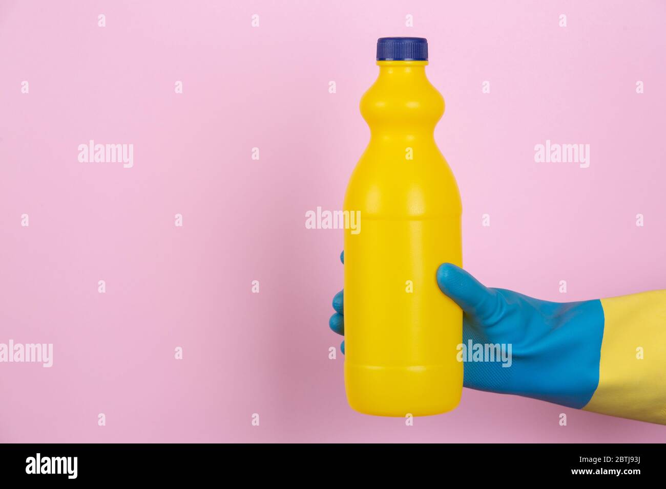 Una mano con guanti per la pulizia che tengono una bottiglia di candeggina su sfondo rosa Foto Stock