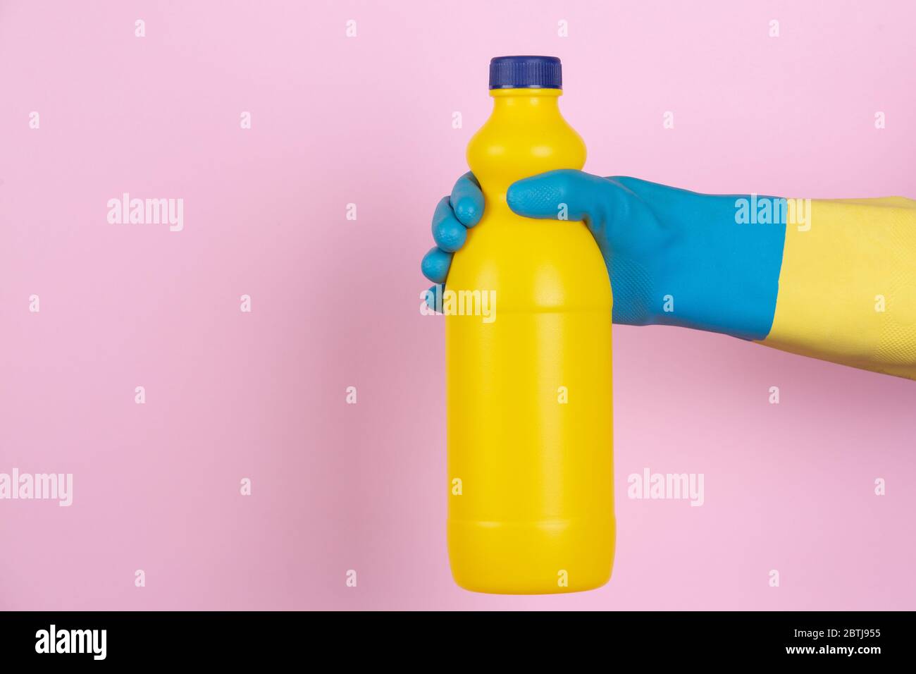 Una mano con guanti per la pulizia che tengono una bottiglia di candeggina su sfondo rosa Foto Stock