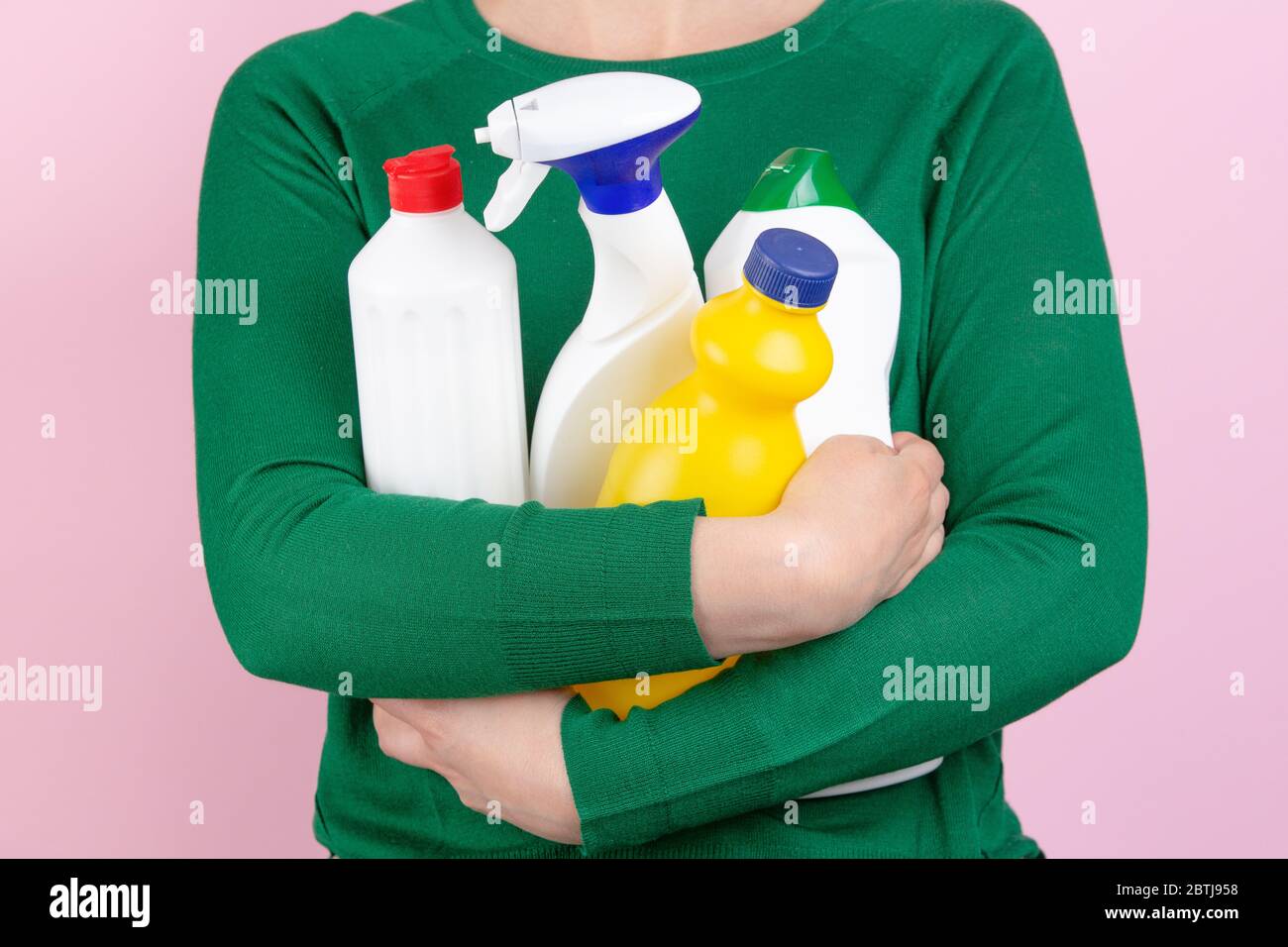 donna con maglione verde e sfondo rosa che abbruttano molti prodotti per la pulizia nelle braccia Foto Stock