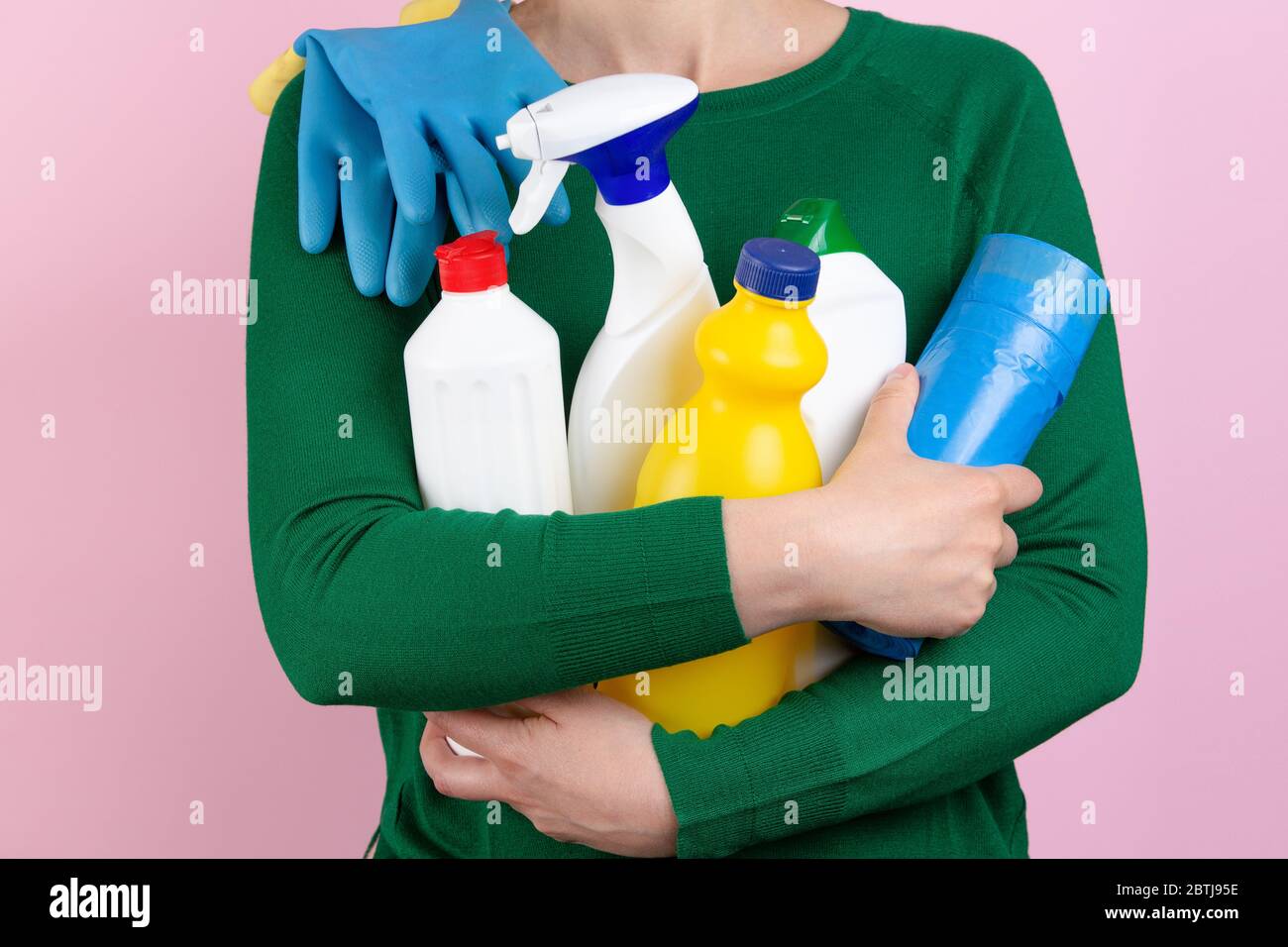 donna con maglione verde e sfondo rosa che abbruttano molti prodotti per la pulizia nelle braccia Foto Stock