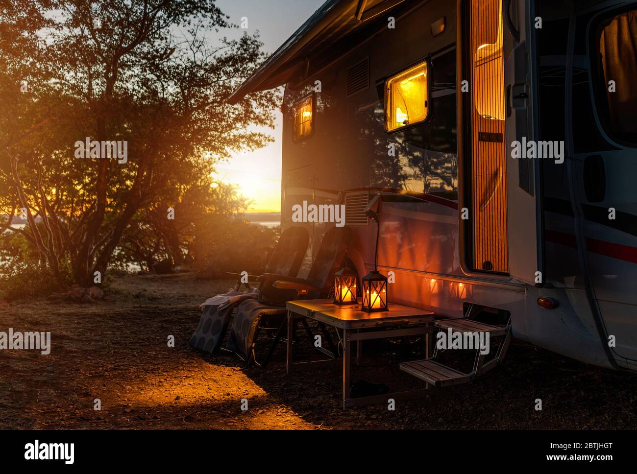 Avventure di viaggio su strada. Notte calda calma su un campeggio. Camper, sedie da esterno e luce romantica dalle Lanterne. Vacanza in veicolo da diporto. Foto Stock
