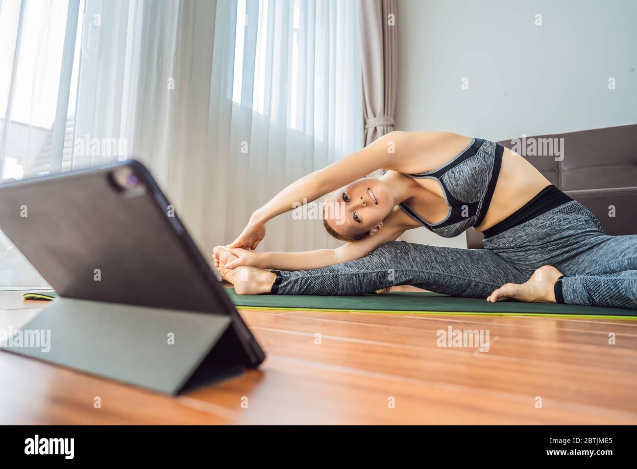 Donna che si esercita sul pavimento a casa e guarda i video di fitness in un tablet. La gente fa sport in linea a causa del coronovirus Foto Stock