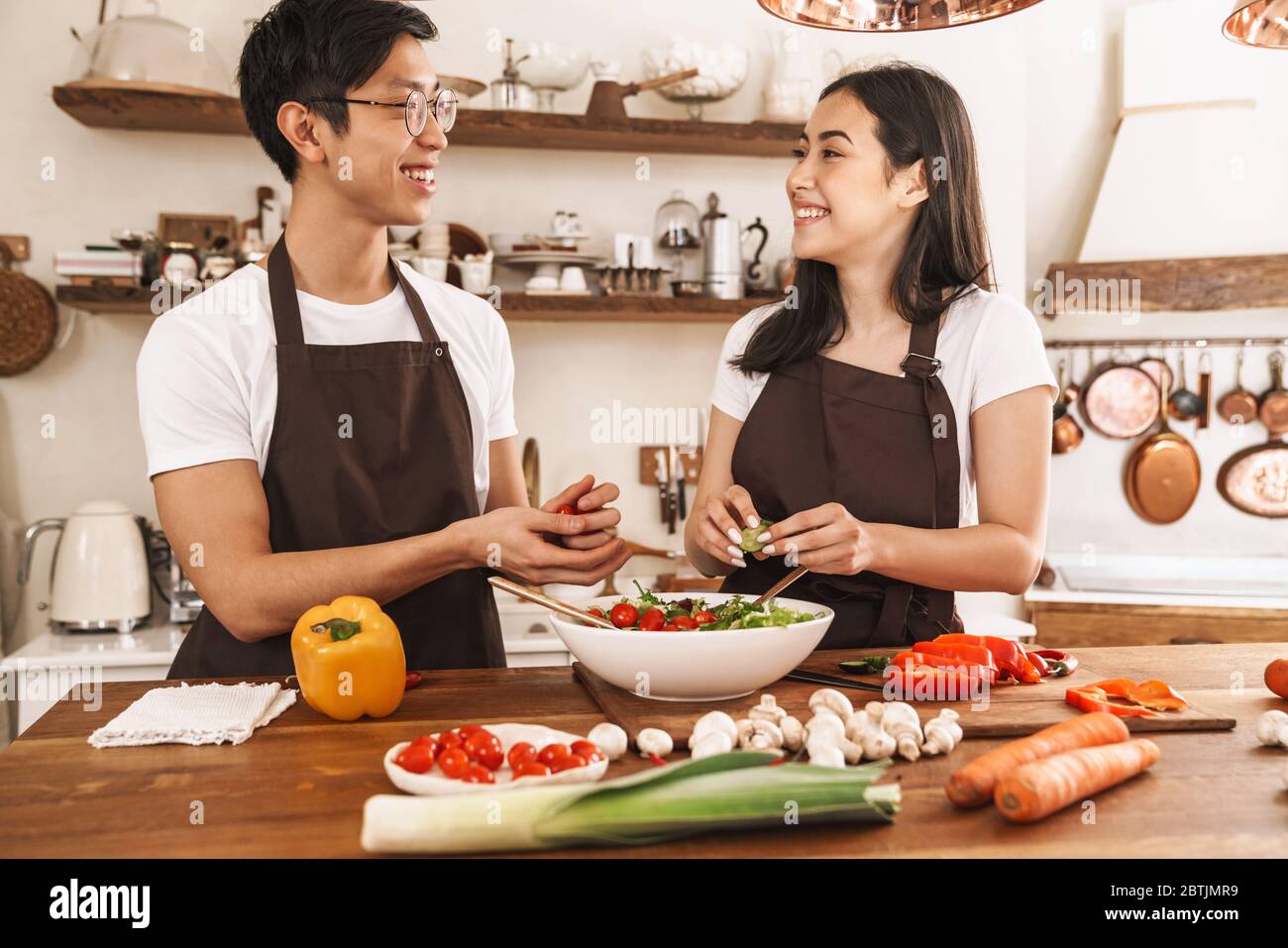 Immagine di una coppia multiculturale sorridente e che guarda su di voi mentre cucinando la cena in una cucina accogliente Foto Stock
