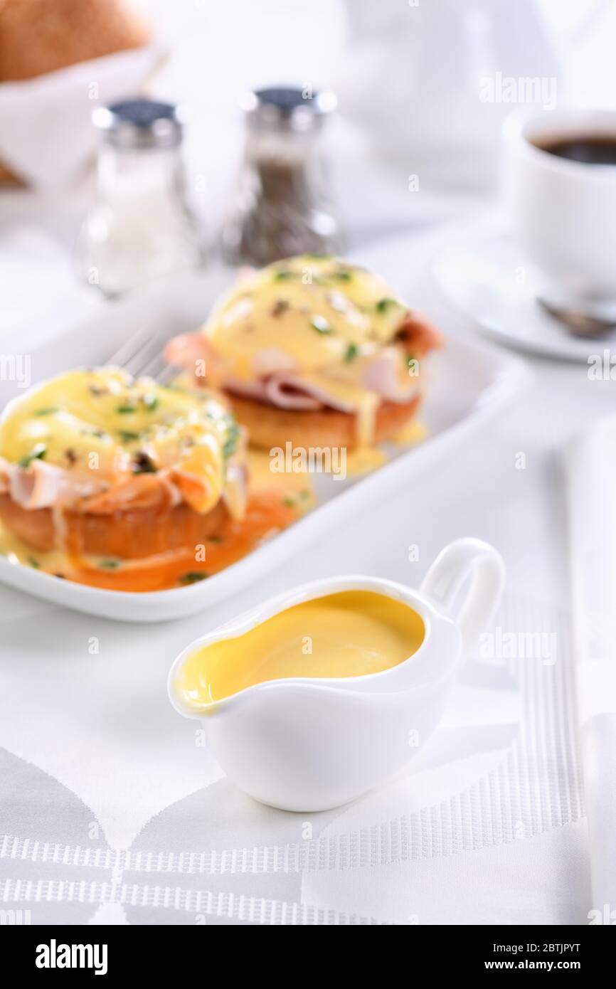 Salsa di burro Hollandaise in una barca con sugo di carne per la colazione servita con uova cucinate alla Benedict, prosciutto, uova in camicia, una tazza di caffè Foto Stock