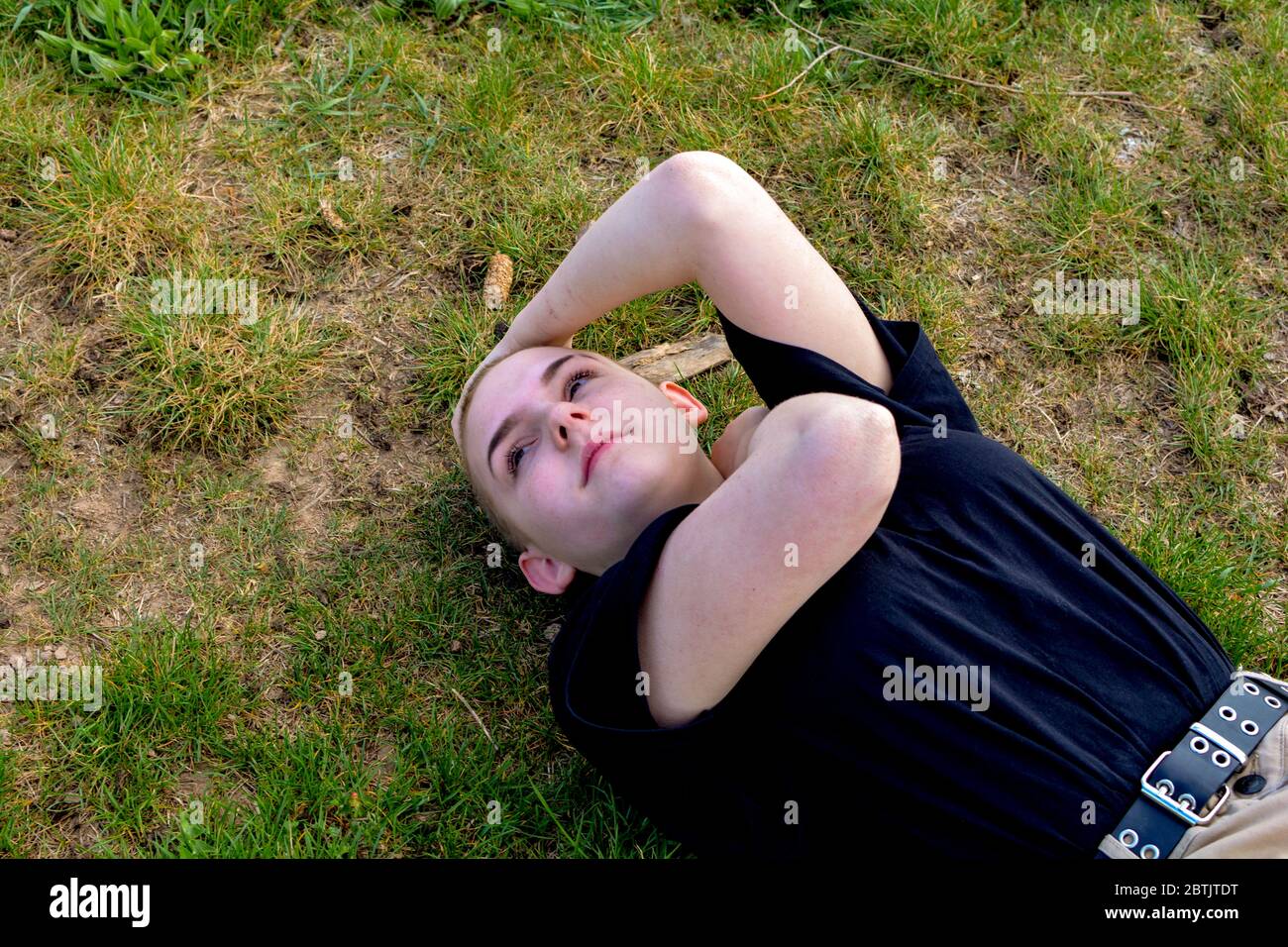Giovane donna con capelli molto corti si trova nell'erba verde, braccia sul collo e la testa Foto Stock