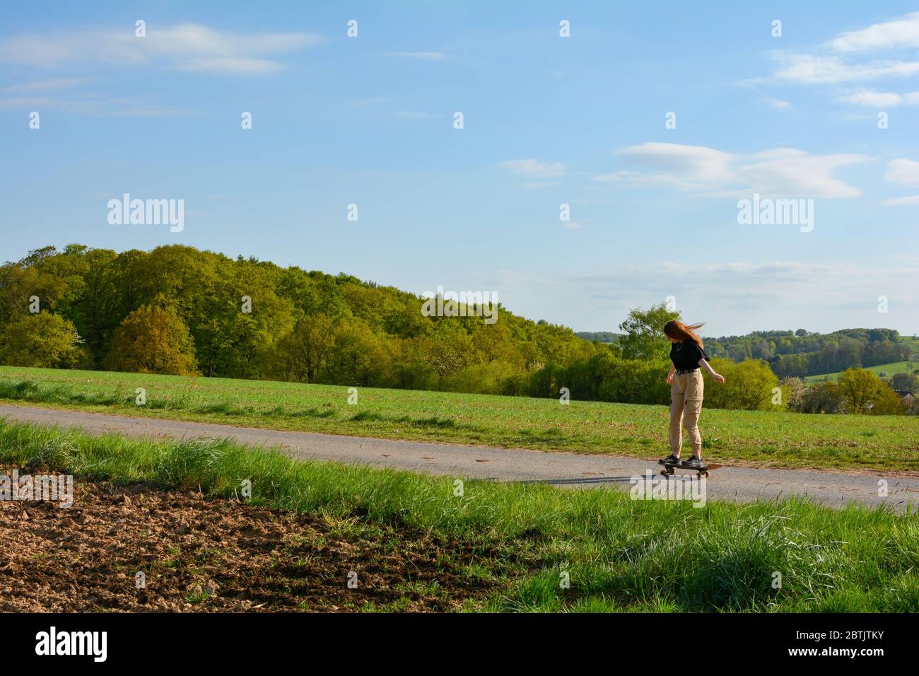 Una ragazza guida uno skateboard su una strada di campagna in natura verde Foto Stock