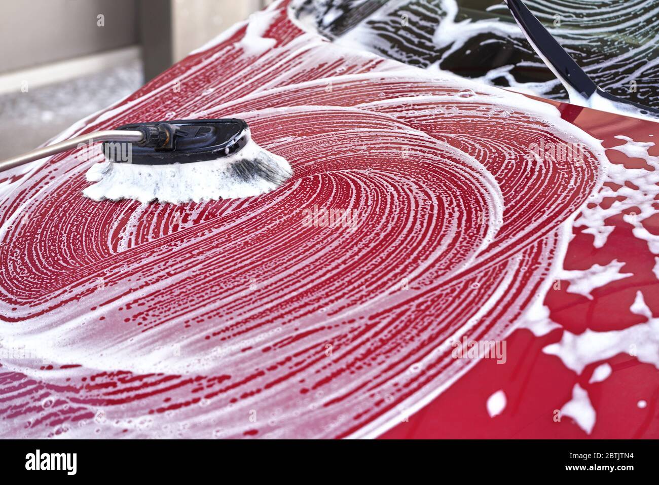 Cappuccio anteriore auto rosso lavato in autolavaggio, dettaglio sulla spazzola lasciando colpi in schiuma di sapone bianco Foto Stock