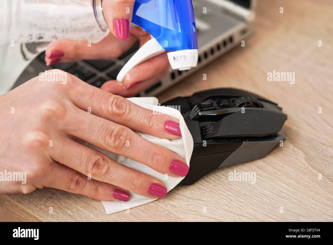 Donna che pulisce il mouse nero del calcolatore, circa spruzzare disinfettare su esso, trattenendo indietro con carta tessuto, dettaglio del closeup sulle mani con le unghie rosa Foto Stock