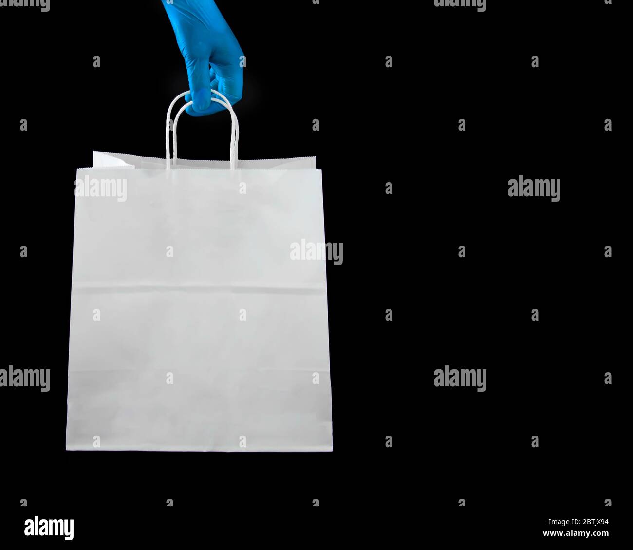 Una persona che indossa guanti di lattice protettivi che tiene una borsa di carta per la spesa Foto Stock