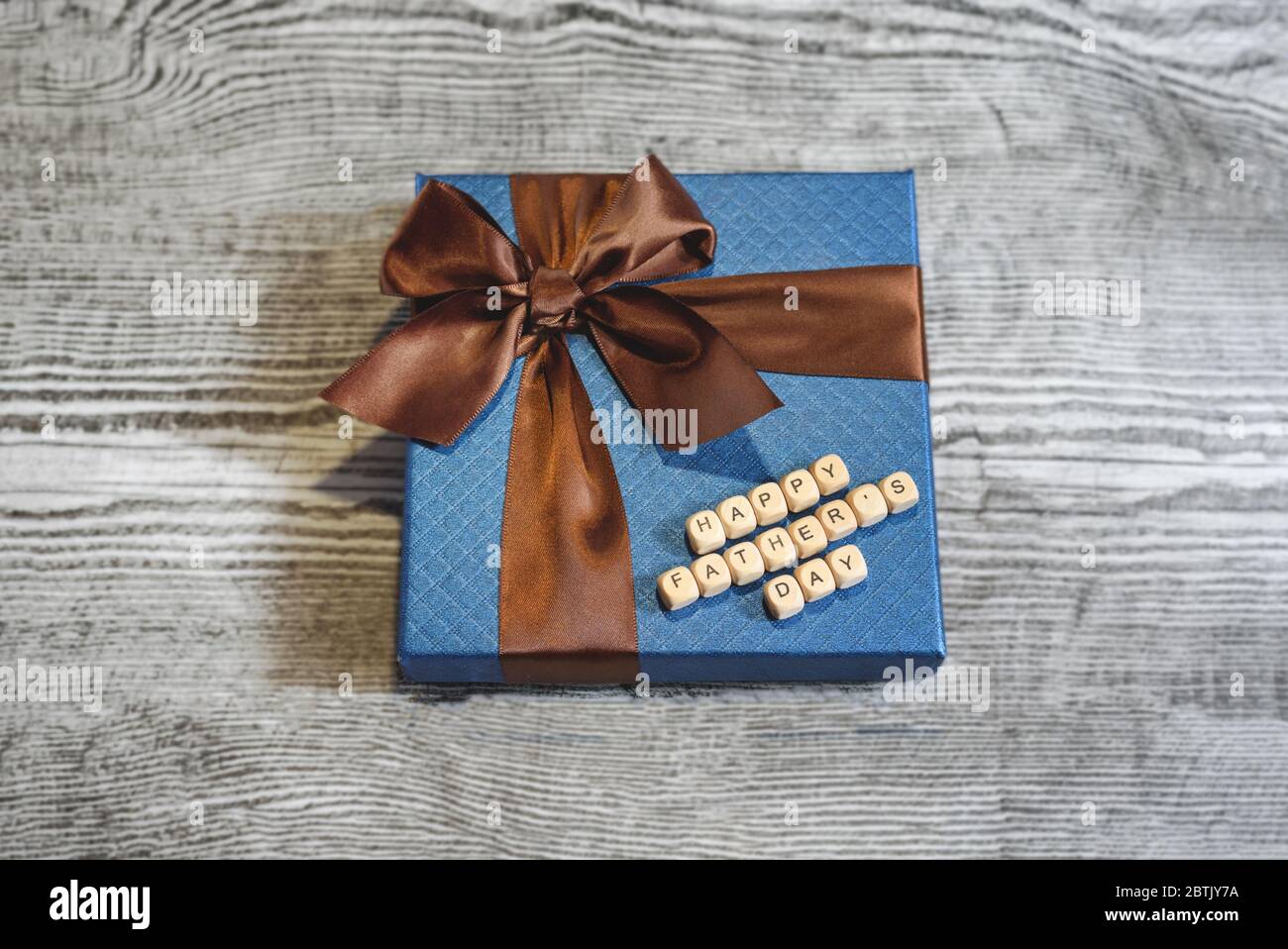 Un regalo blu con striscia marrone su sfondo di legno. Un segno di buon giorno del Padre da blocchi di legno. Concetto di festa del Padre. Foto Stock