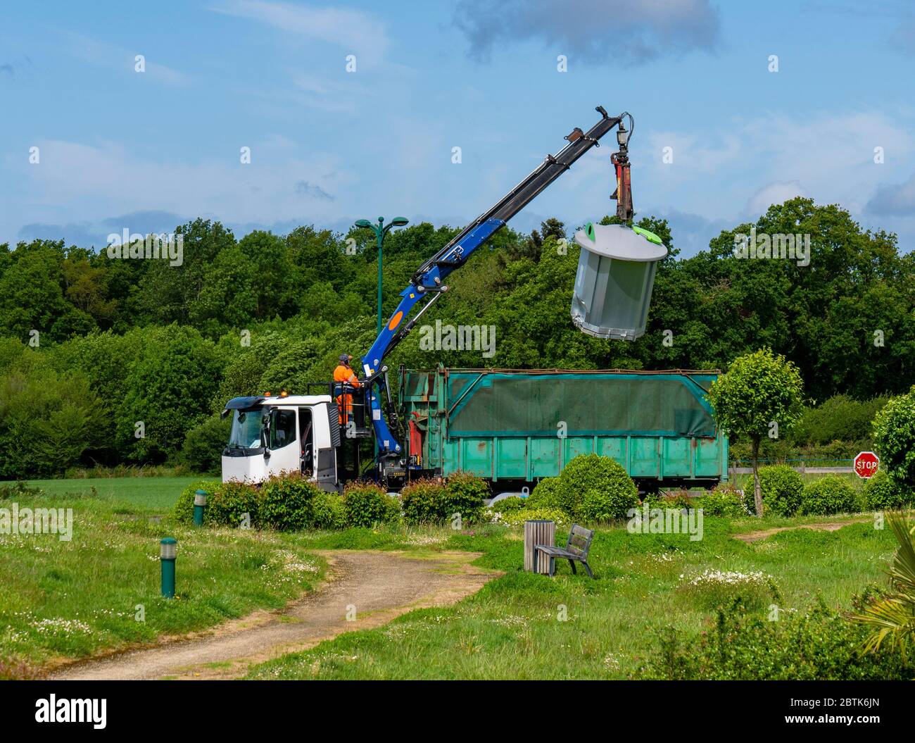 L'operatore del veicolo per raccolta rifiuti riceve rifiuti separati da un contenitore. Sullo sfondo un paesaggio verde con alberi e un sentiero. Foto Stock