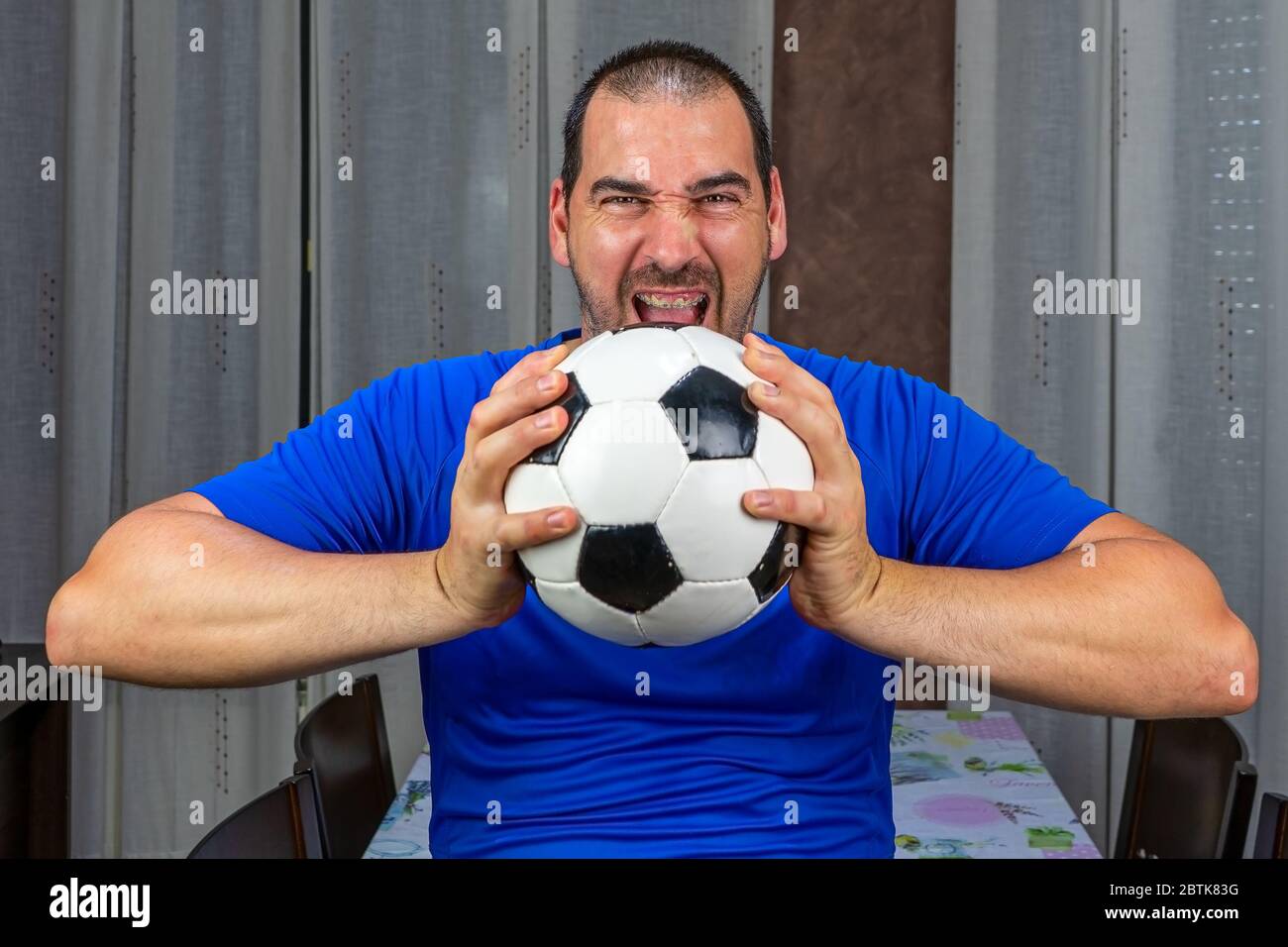 Uomo bearded con i capelli corti in una camicia blu schiacciando grily una sfera di calcio. Concetto di rabbia Foto Stock