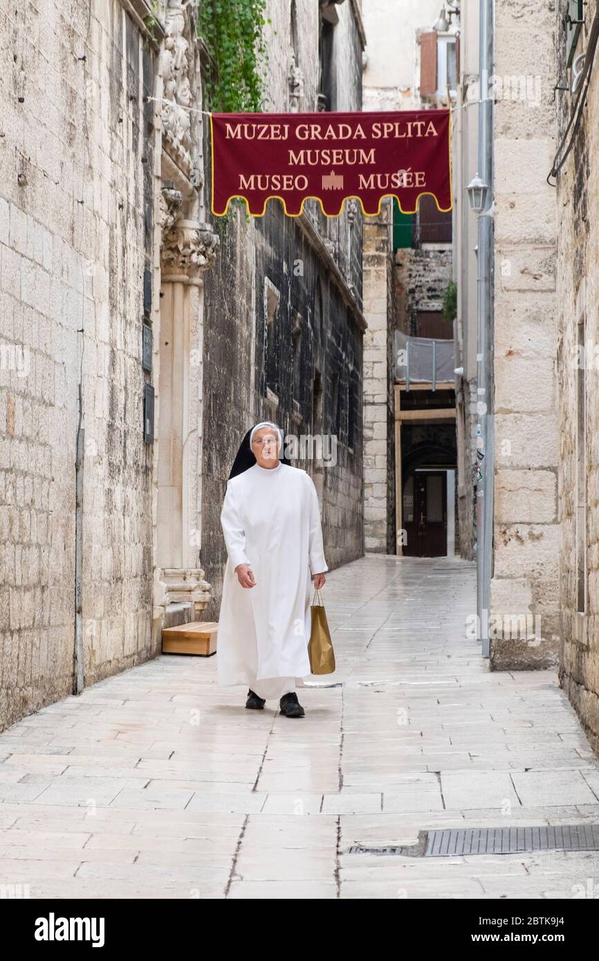 Una suora in abitudine tradizionale cammina attraverso una stretta passerella vicino al Museo Muzej Grada Splita, la Città Vecchia, Spalato, Croazia Foto Stock