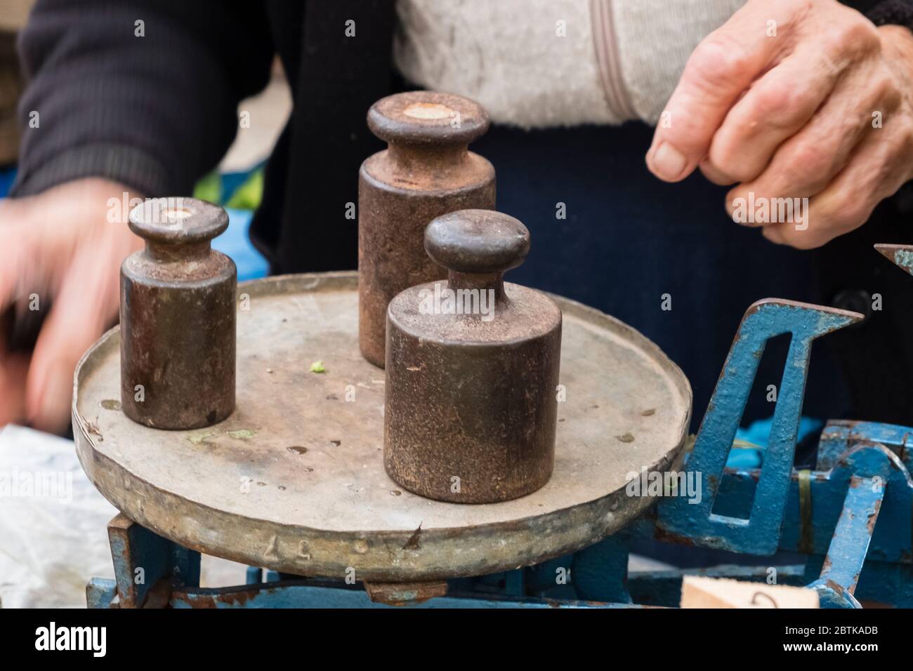 Il venditore di strada femminile più anziano usa una vecchia scala meccanica con i vecchi pesi di metallo per pesare frutta e verdura per la vendita, al mercato verde di Spalato, Croazia Foto Stock