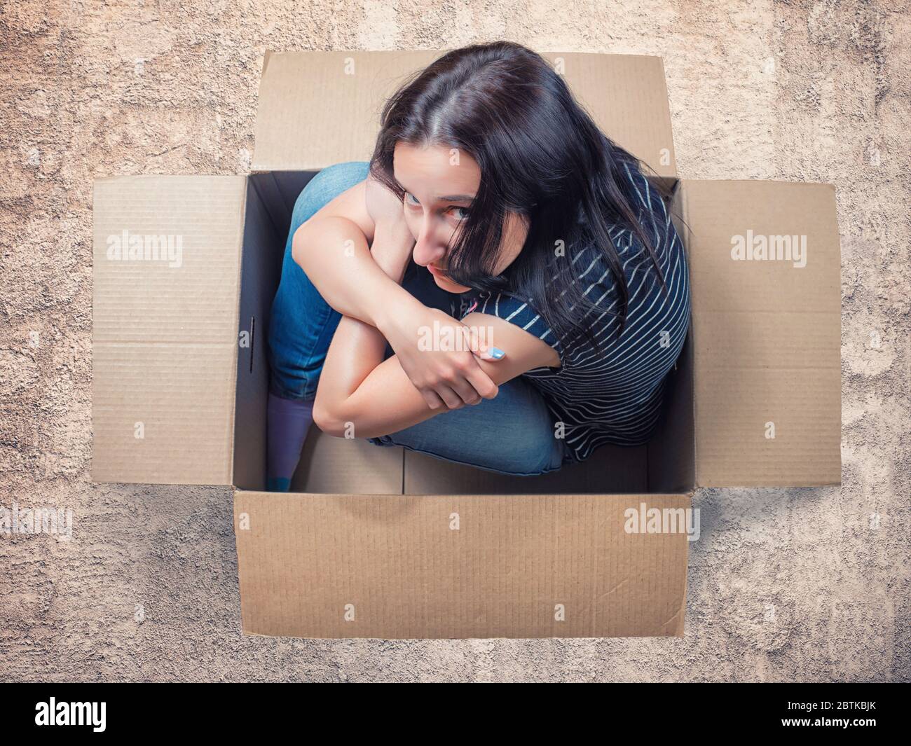 Donna seria seduta in scatola di cartone su pavimento ruvido. Spazio personale, isolamento, introfersione e tema di ansia Foto Stock