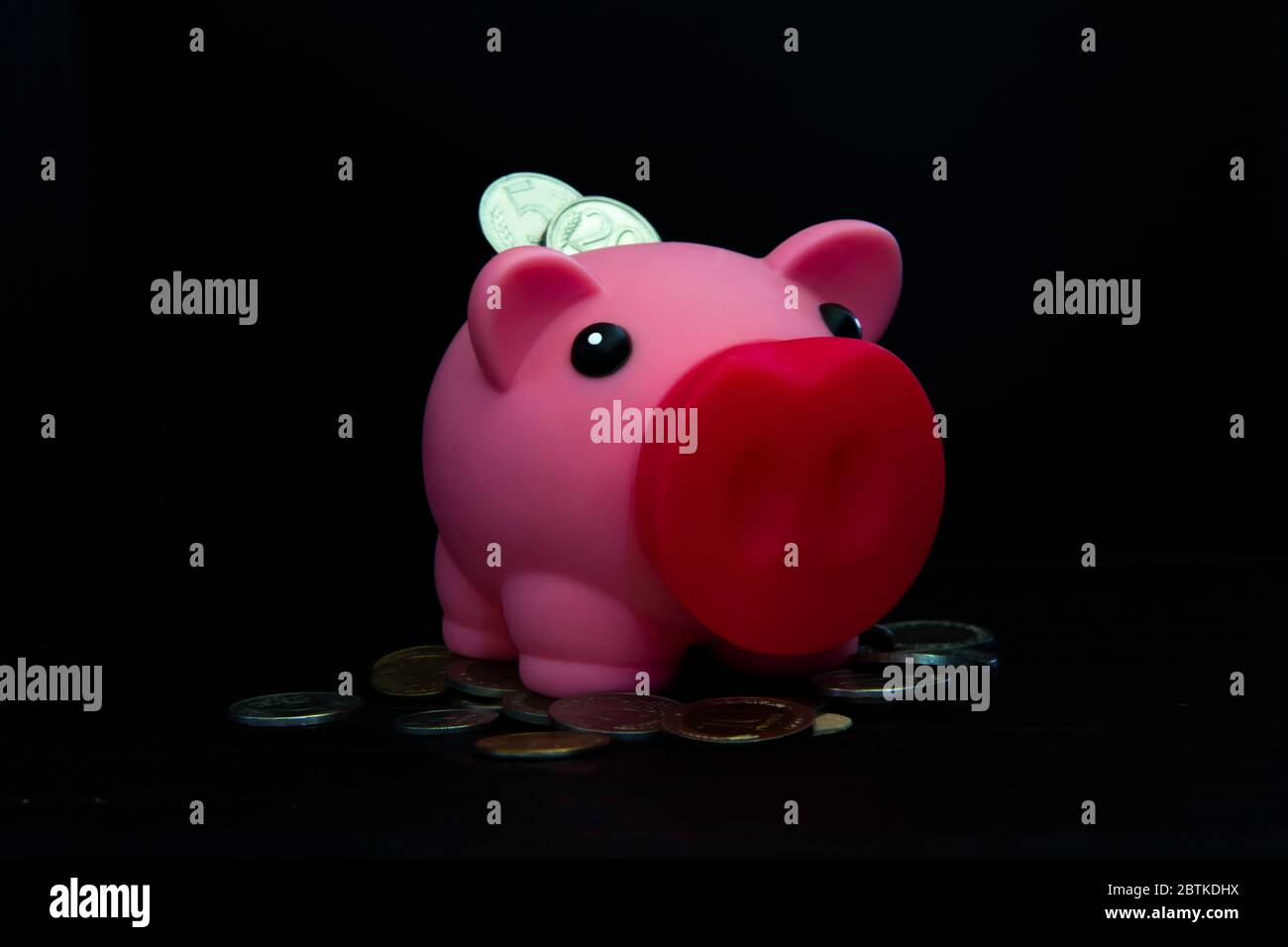 Rosa piggy banca piena di monete su uno sfondo nero. Concetto di dove investire i vostri risparmi. Fare soldi Foto Stock