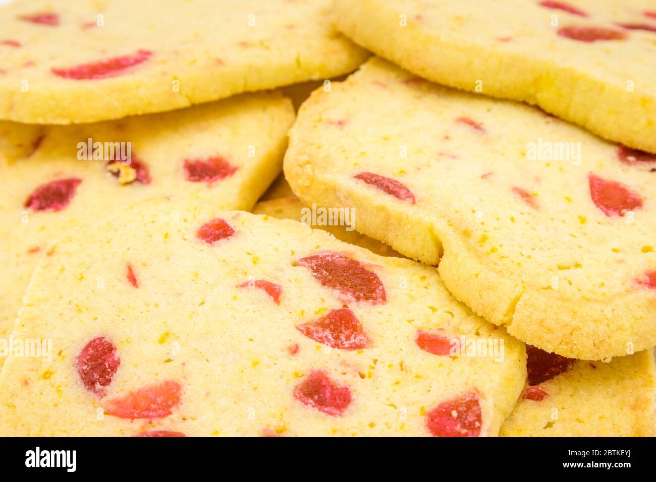 Vista ravvicinata di un mucchio di tradizionali fette croccanti e biscotti al forno, biscotti dorati fatti in casa con pezzi di ciliegia rossa presentati su un piatto bianco Foto Stock