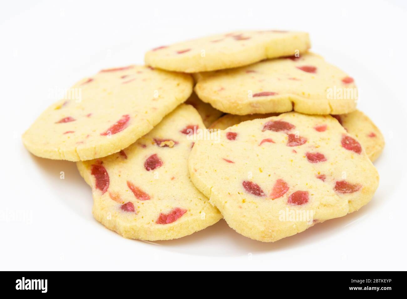 Un mucchio di biscotti tradizionali croccanti a fette e da cuocere, biscotti dorati fatti in casa con pezzi di ciliegia rossa presentati su un piatto bianco Foto Stock