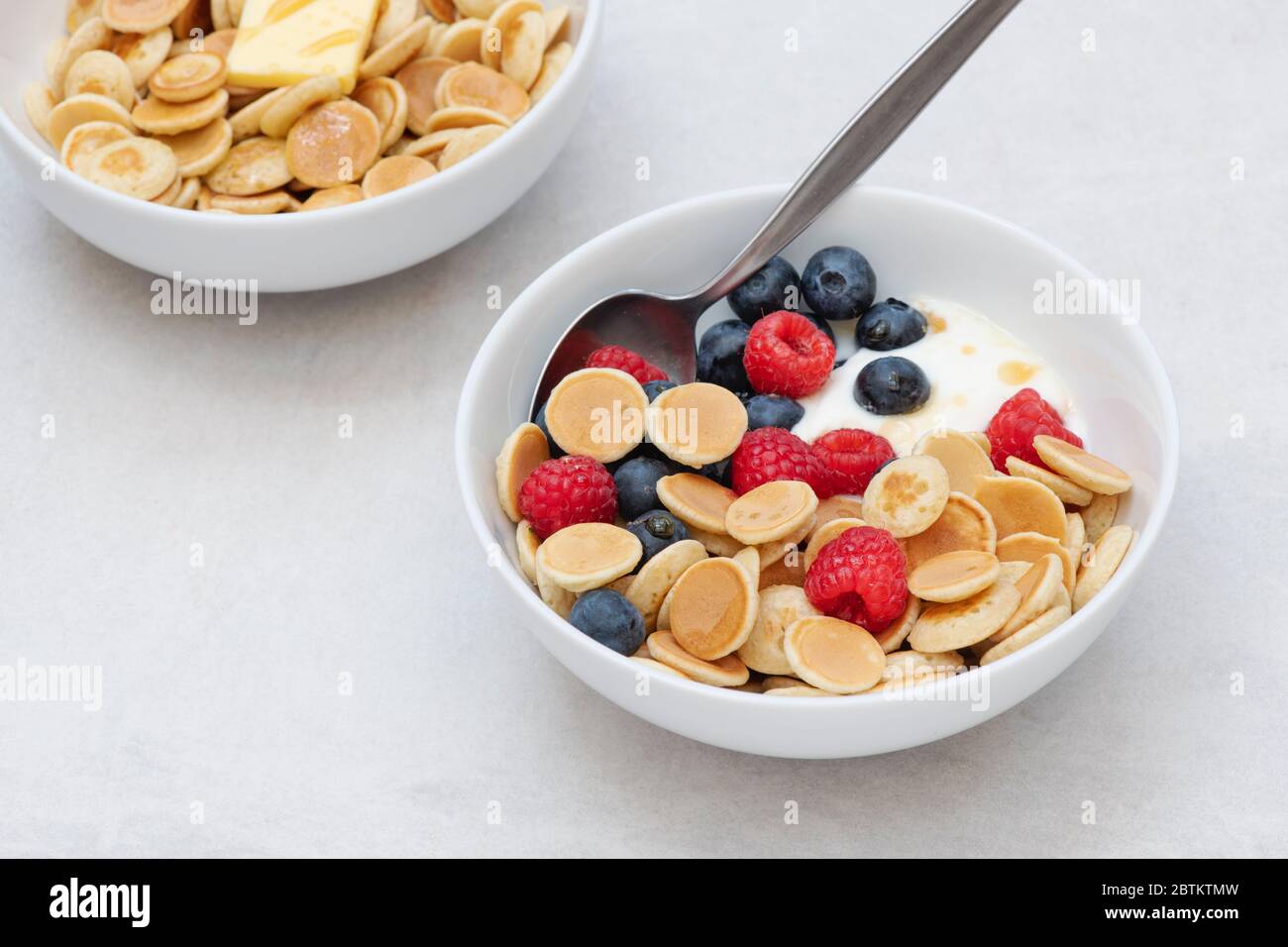 Ciotola di frittelle di cereali con mirtilli lamponi yogurt e sciroppo d'acero e una ciotola con cereali pancake burro e sciroppo Foto Stock