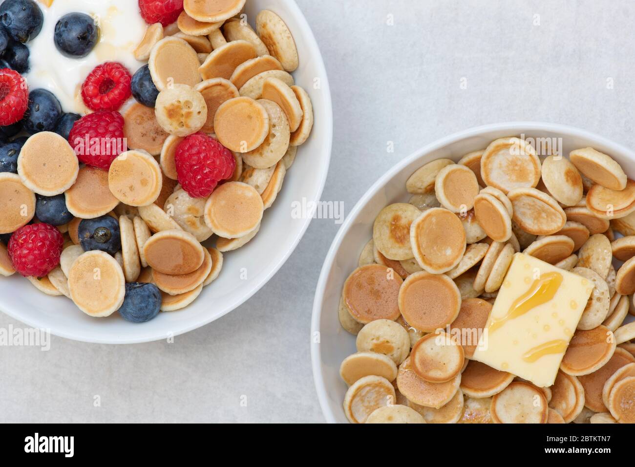Ciotola di frittelle di cereali con mirtilli lamponi yogurt e sciroppo d'acero e una ciotola con cereali pancake burro e sciroppo Foto Stock
