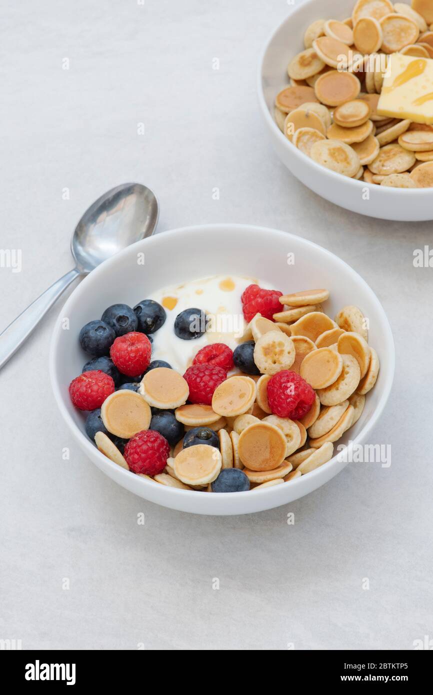 Ciotola di frittelle di cereali con mirtilli lamponi yogurt e sciroppo d'acero e una ciotola con cereali pancake burro e sciroppo Foto Stock