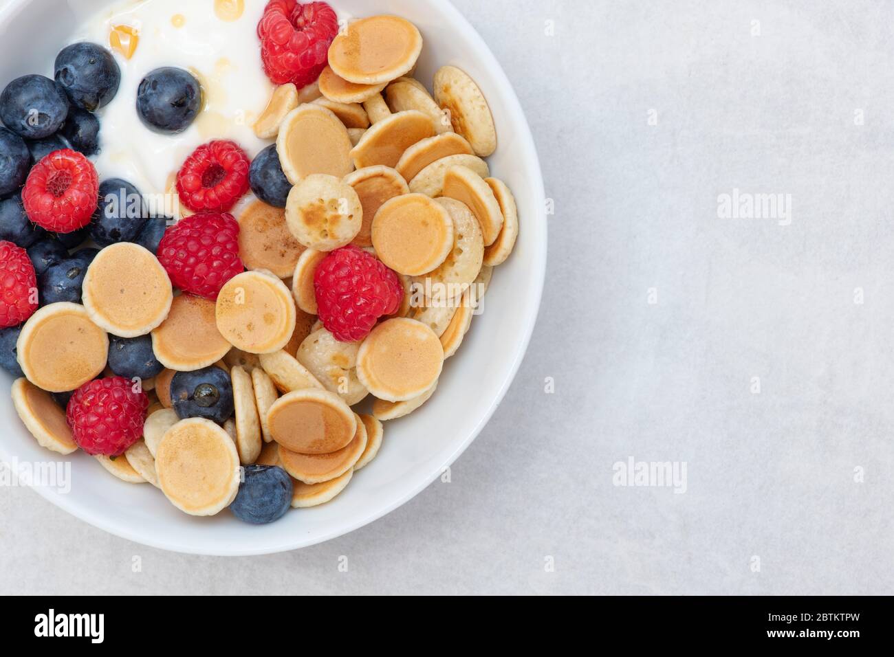Ciotola di frittelle di cereali con mirtilli lamponi yogurt e sciroppo d'acero Foto Stock