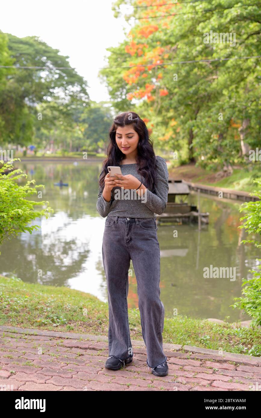 Foto corpo pieno di giovane bella donna indiana utilizzando il telefono al parco all'aperto Foto Stock